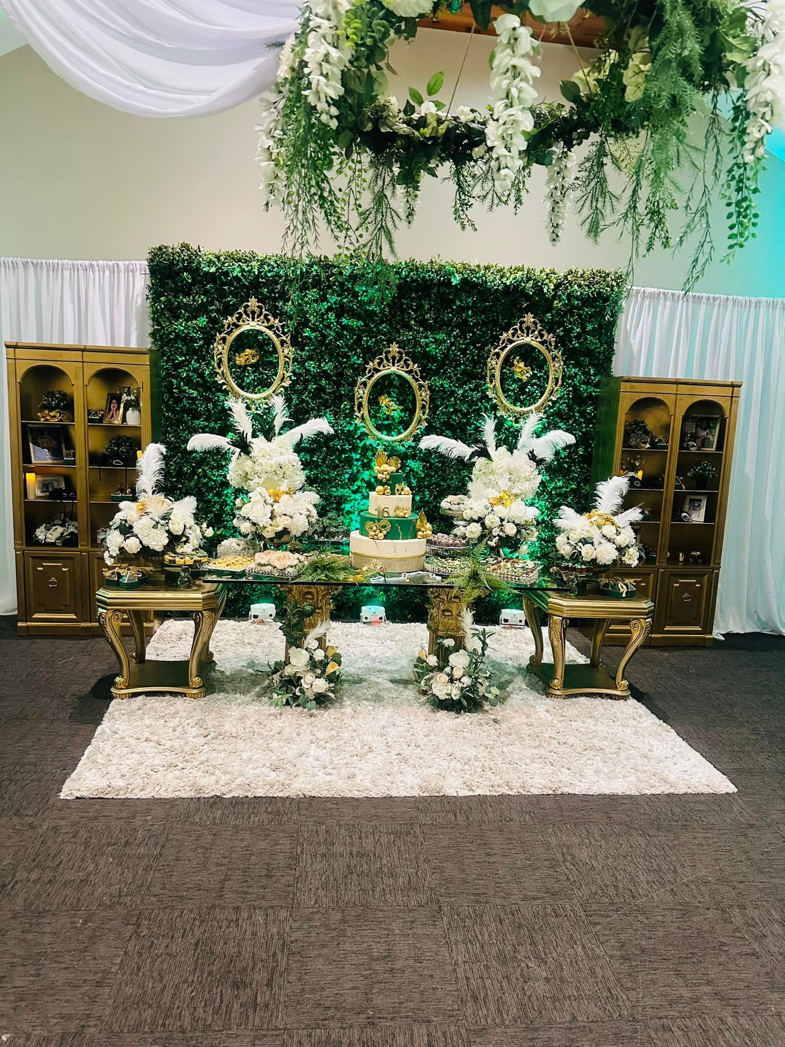 A table with flowers and a cake on it in front of a green wall.