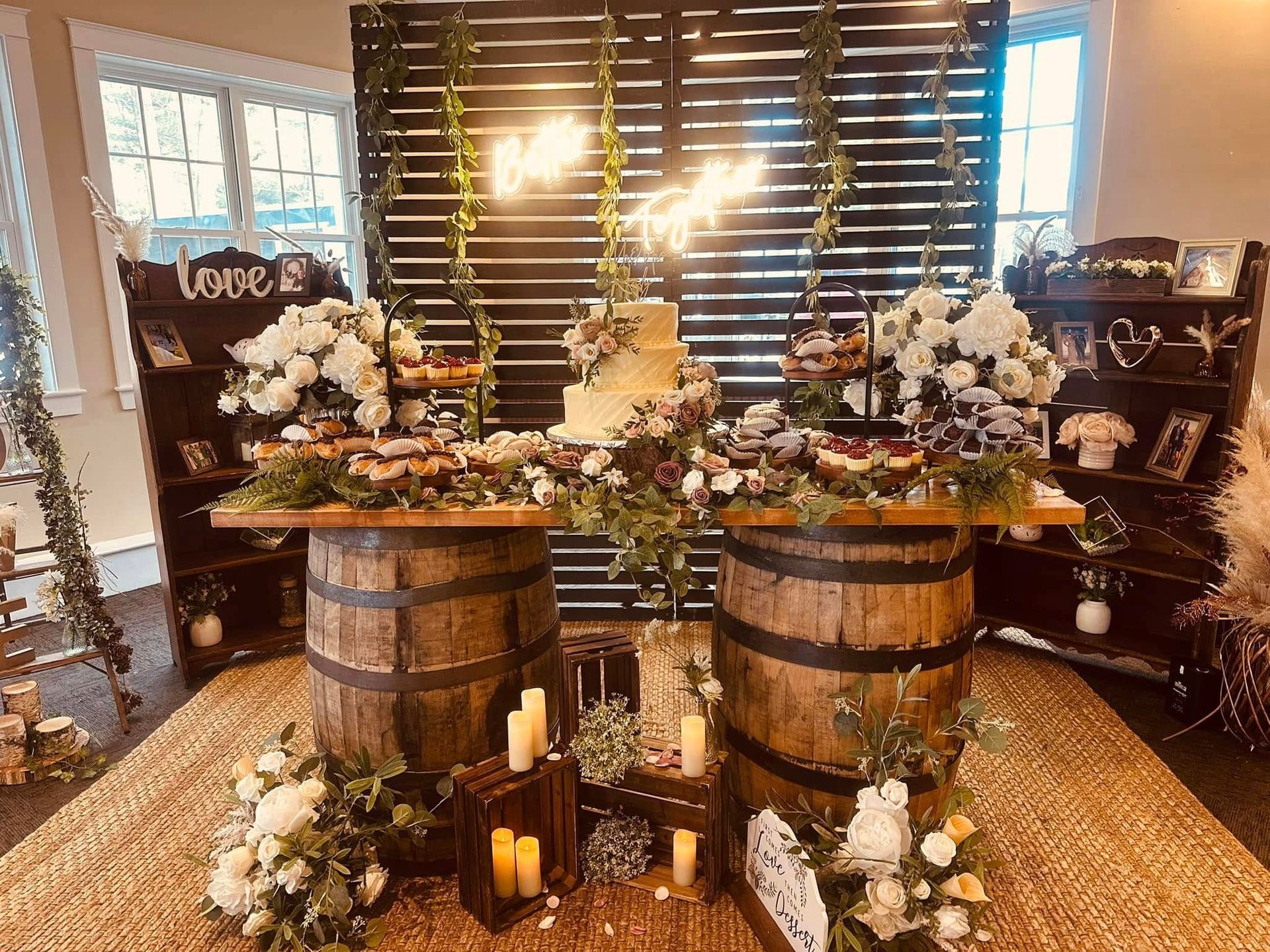 A table with a cake , candles , flowers and barrels in front of a wooden wall.