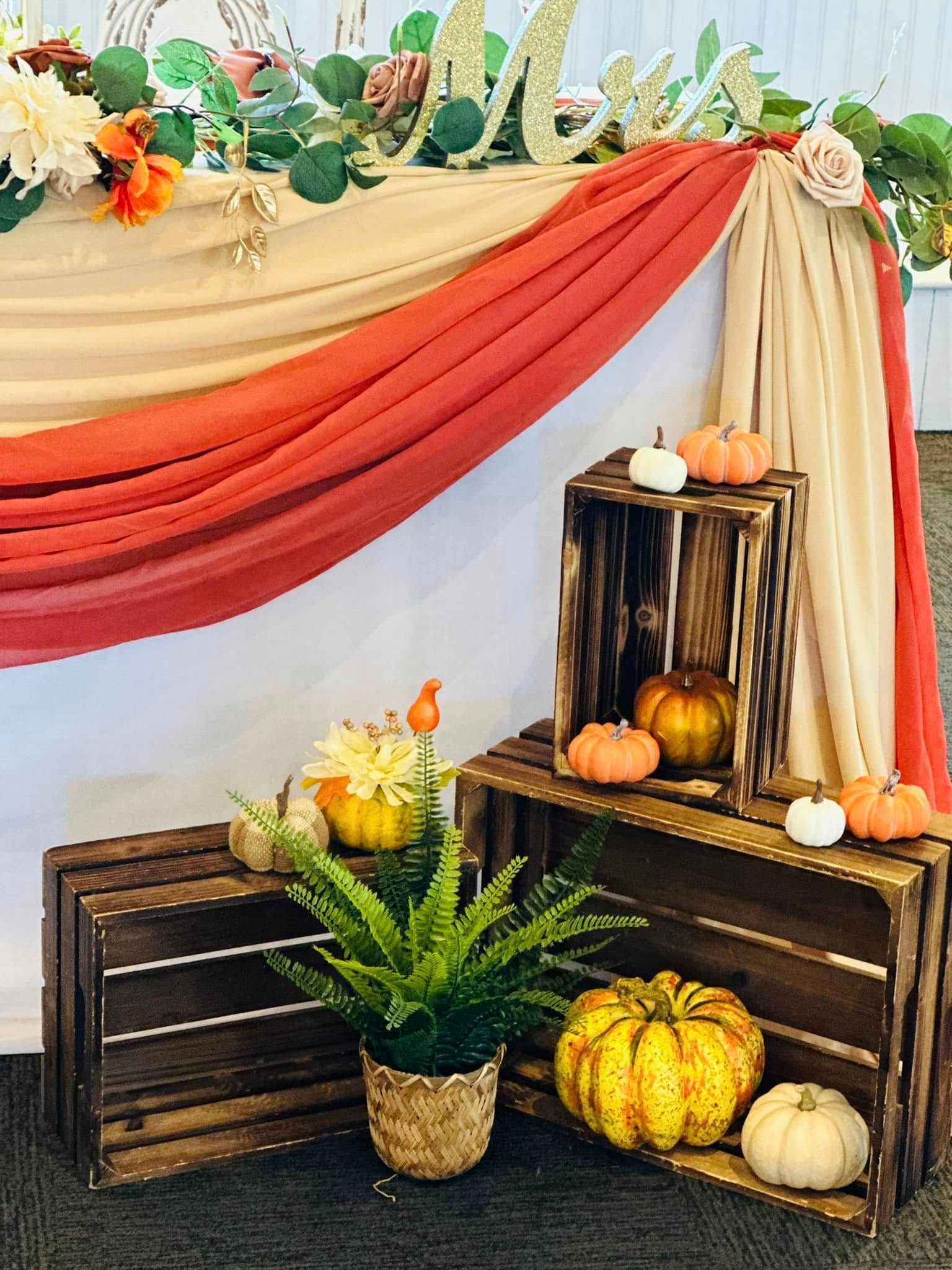 A table with a red curtain and wooden crates filled with pumpkins and flowers.
