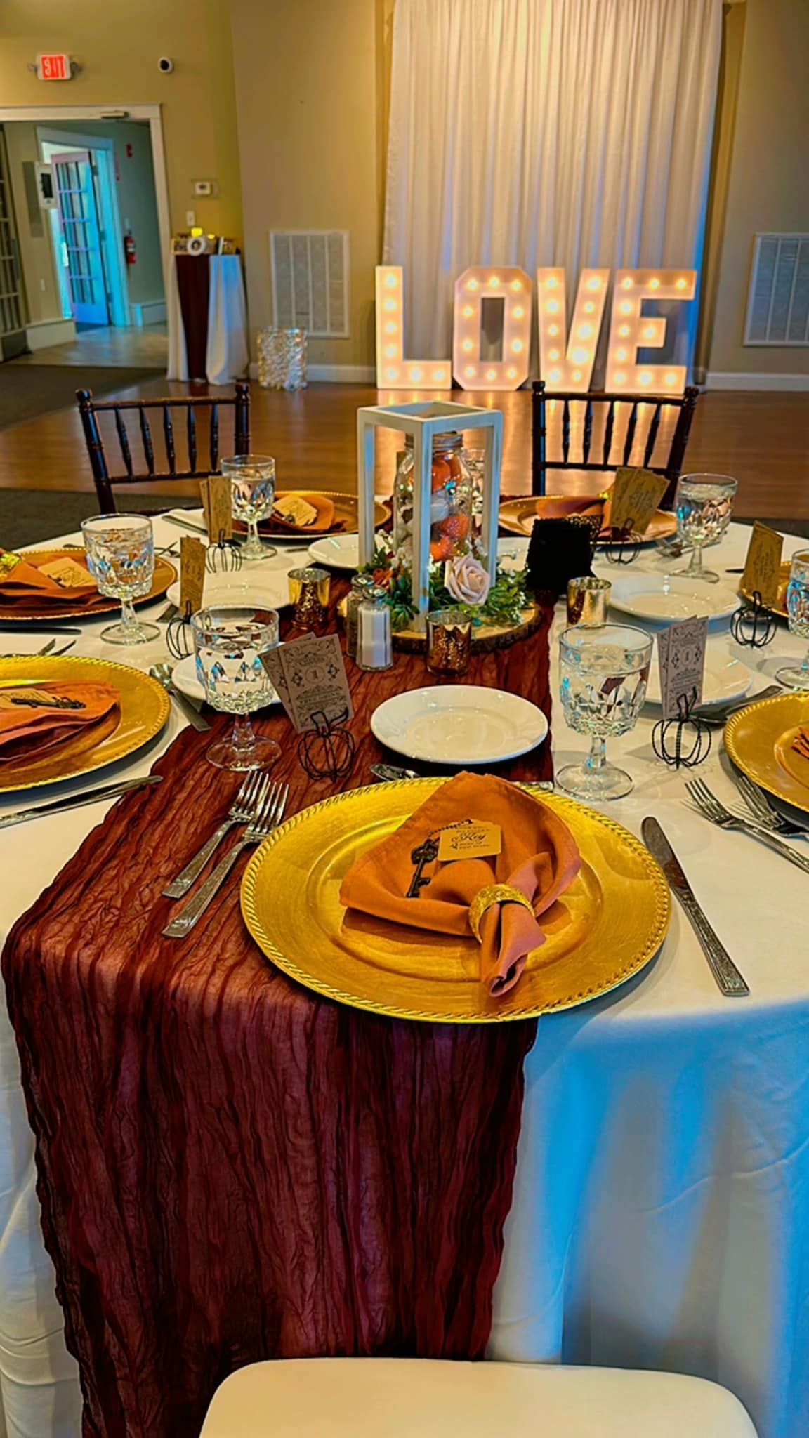A table set for a wedding reception with plates , napkins , utensils and a love sign in the background.