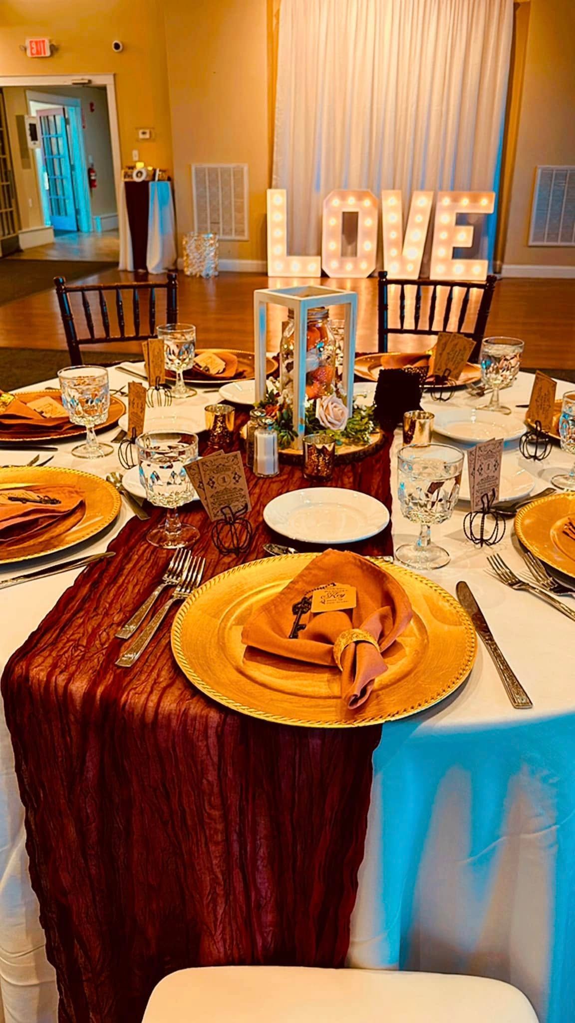 A table set for a wedding reception with plates , utensils , and a love sign in the background.