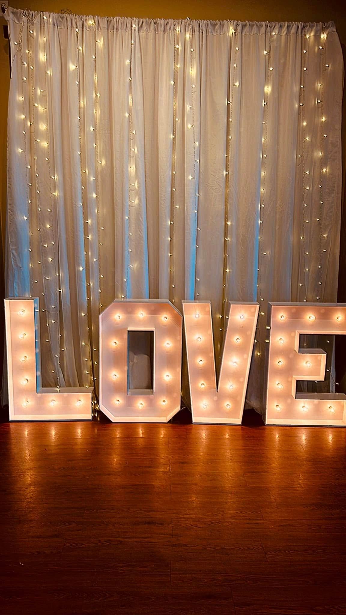The word love is lit up in front of a white curtain.