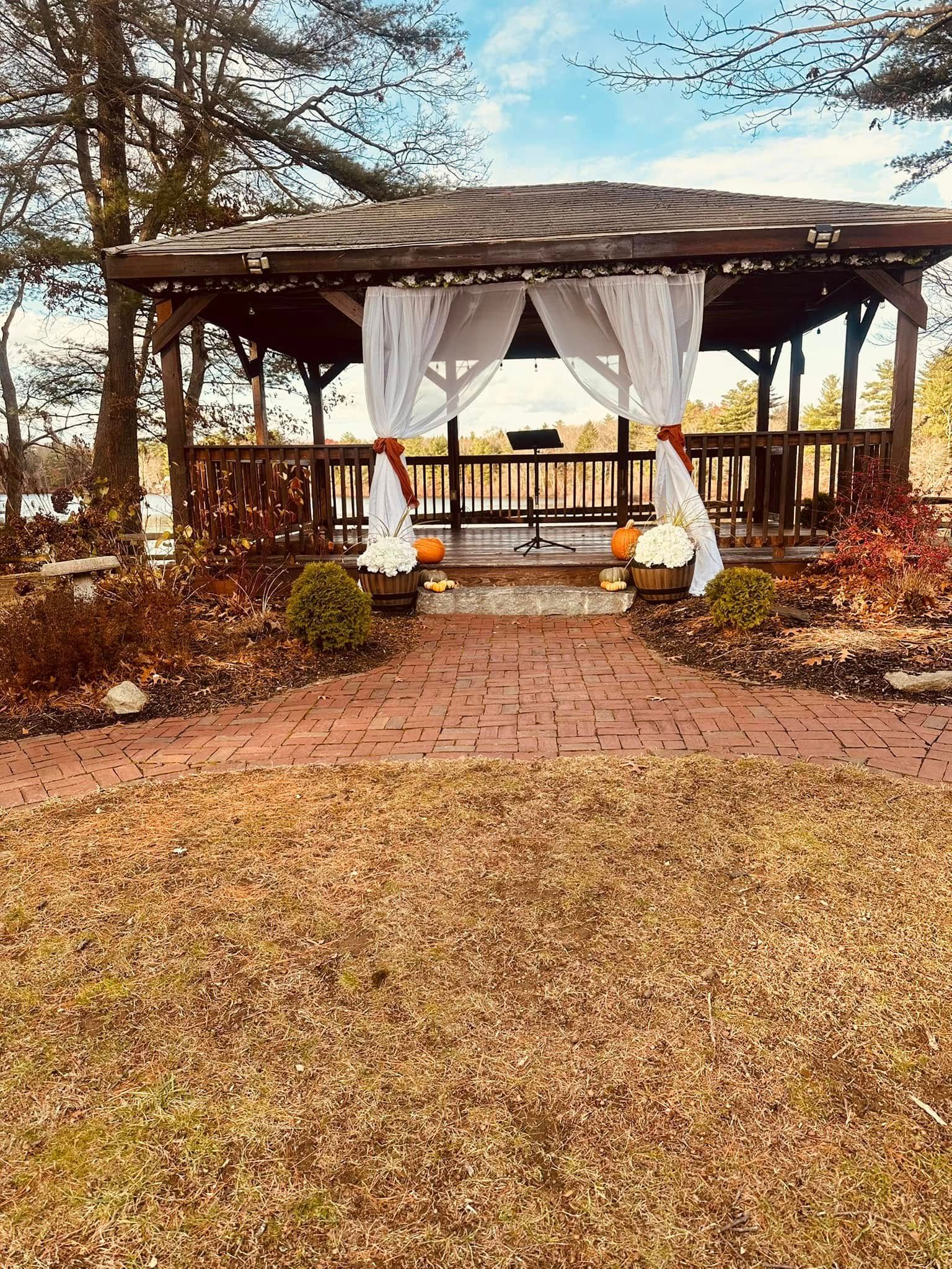 A gazebo with white curtains is sitting in the middle of a lush green field.