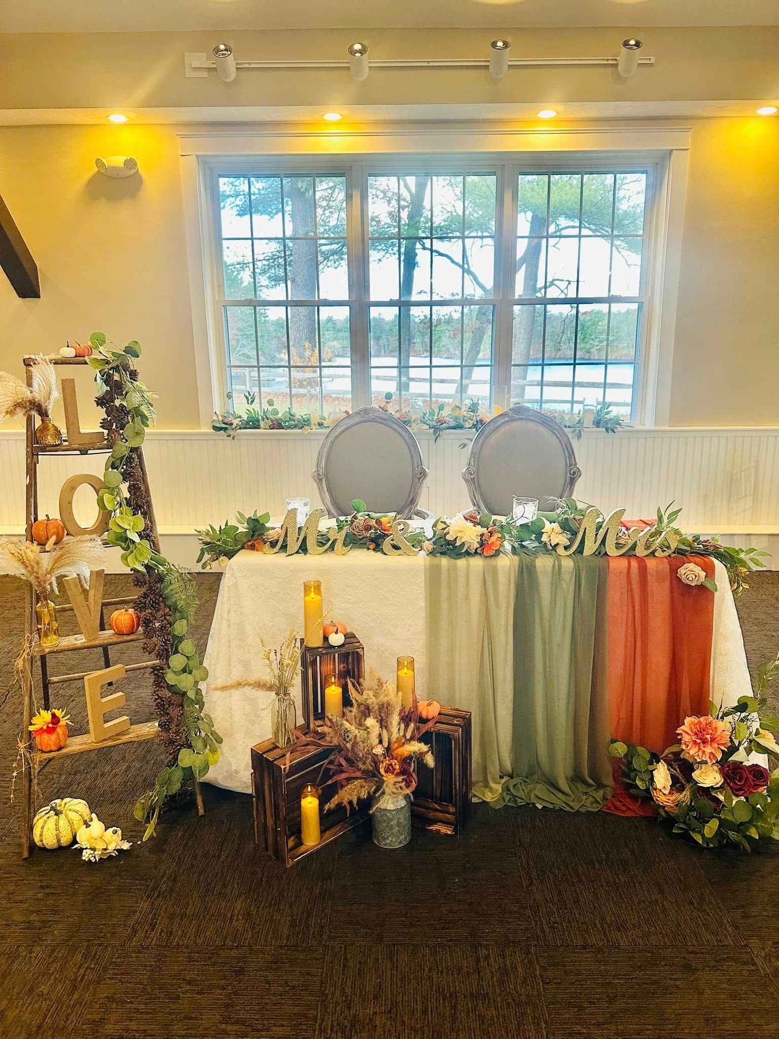 There is a table with flowers and candles on it in front of a window.