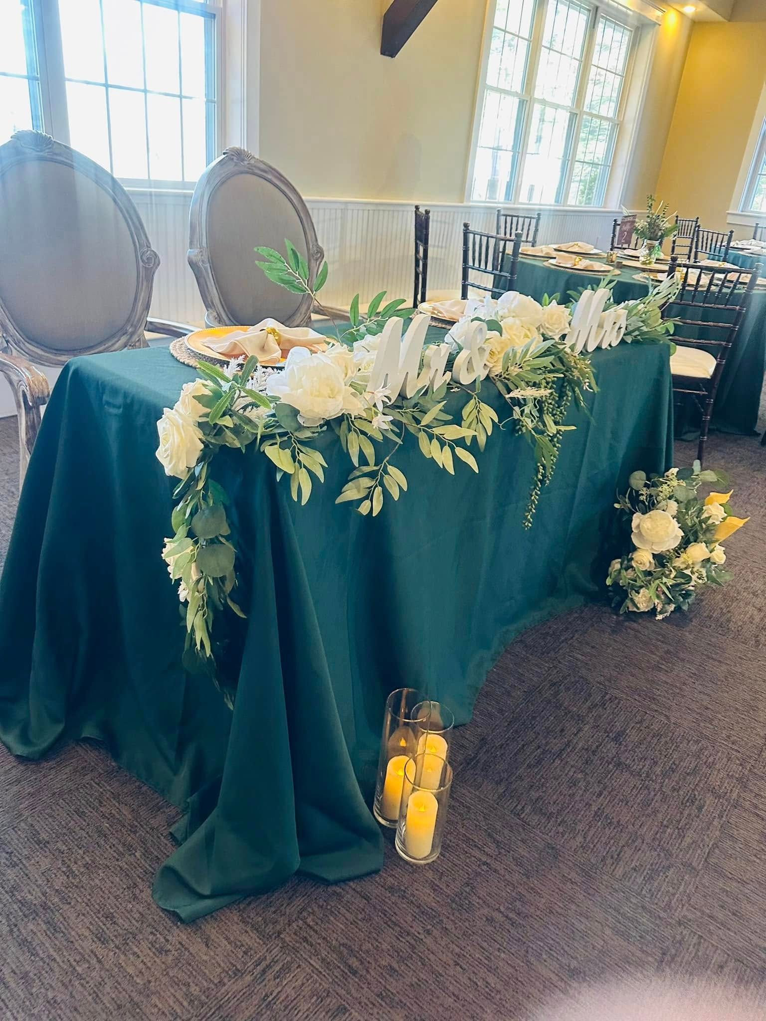 A long green table with flowers and candles on it.