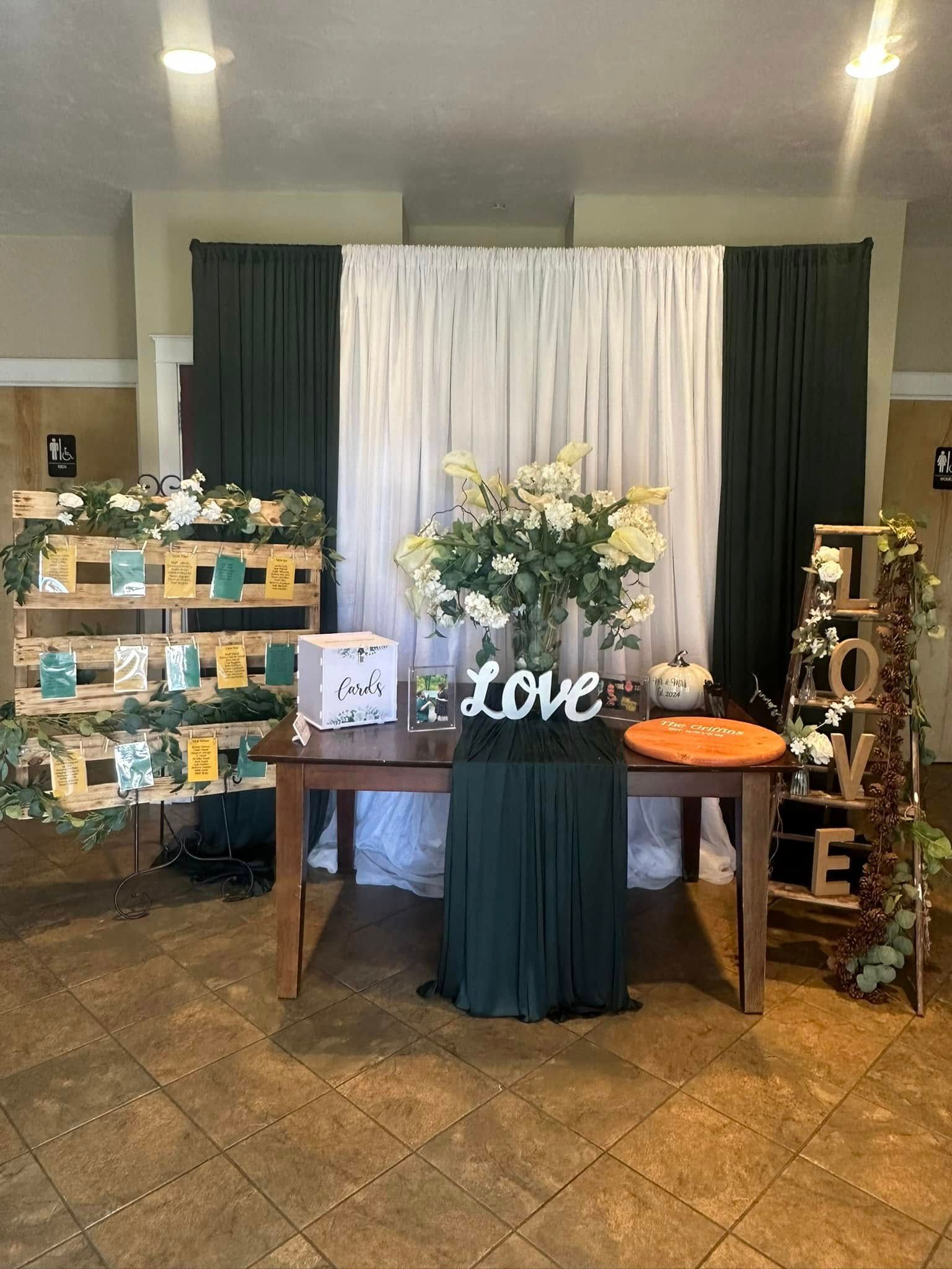 A table with a vase of flowers on it in front of a white curtain.