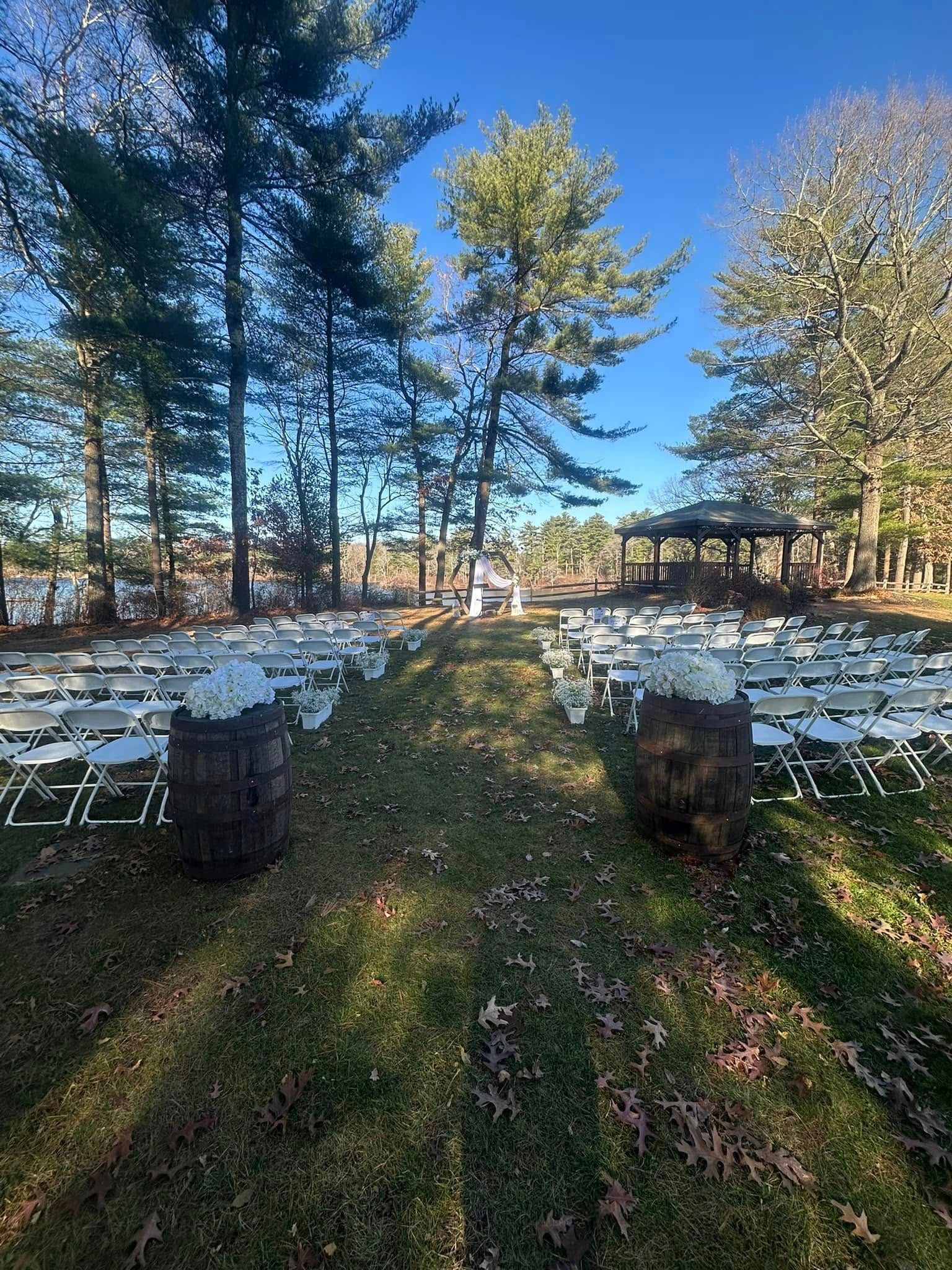 A row of chairs and barrels are lined up in the grass for a wedding ceremony.