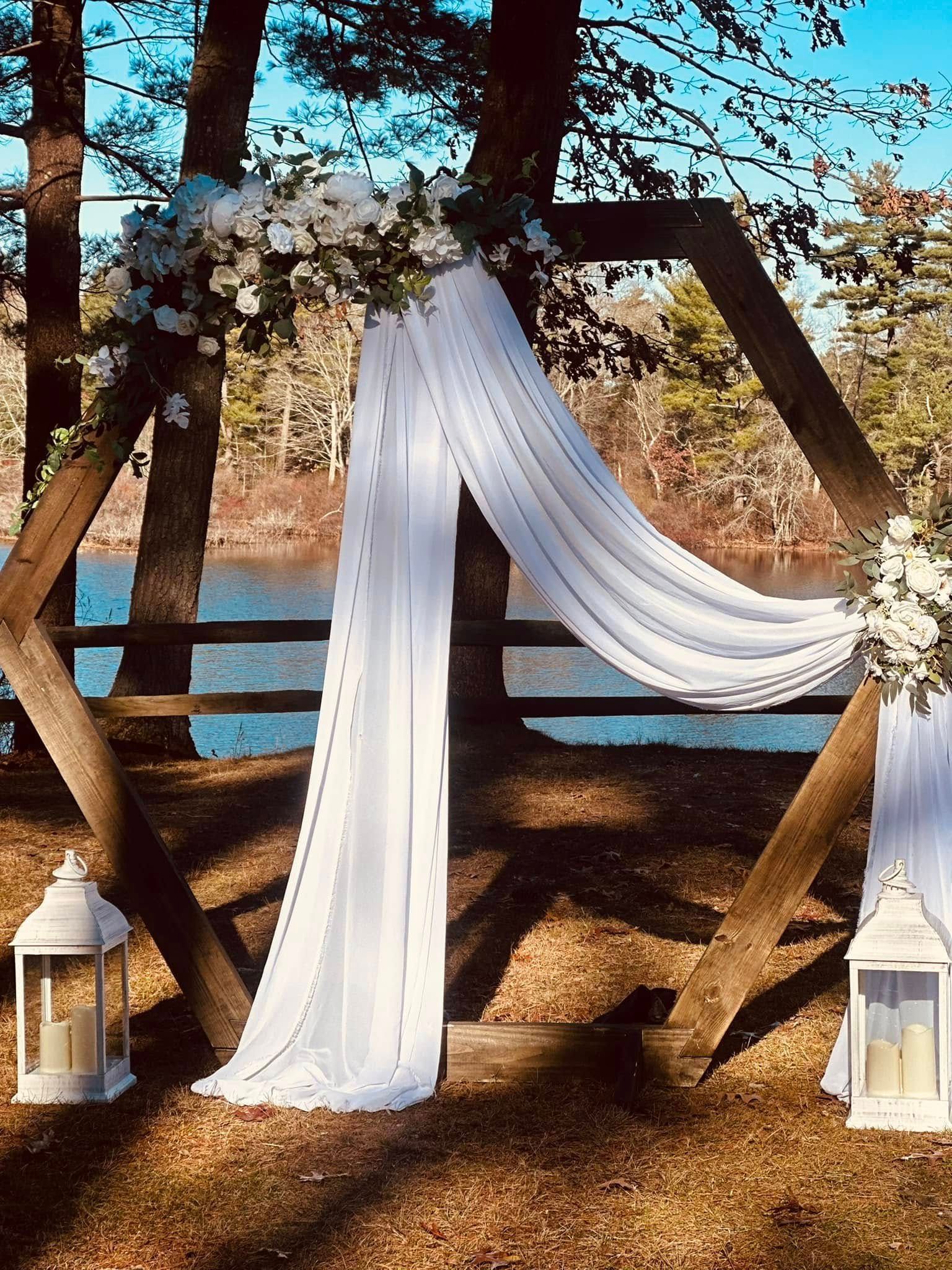 A wooden arch with white flowers and lanterns in front of a lake.