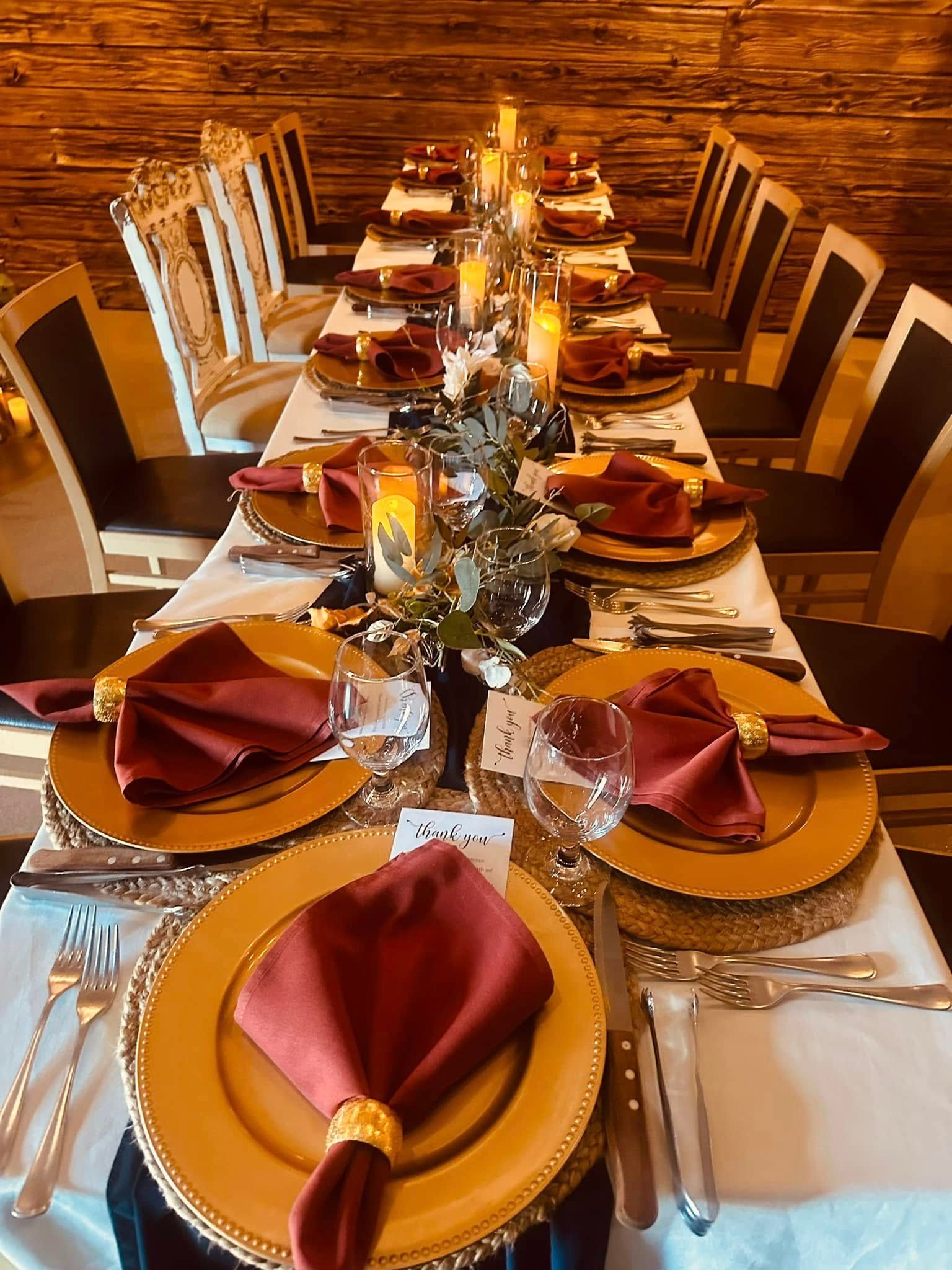 A long table with plates , napkins , candles , and silverware.