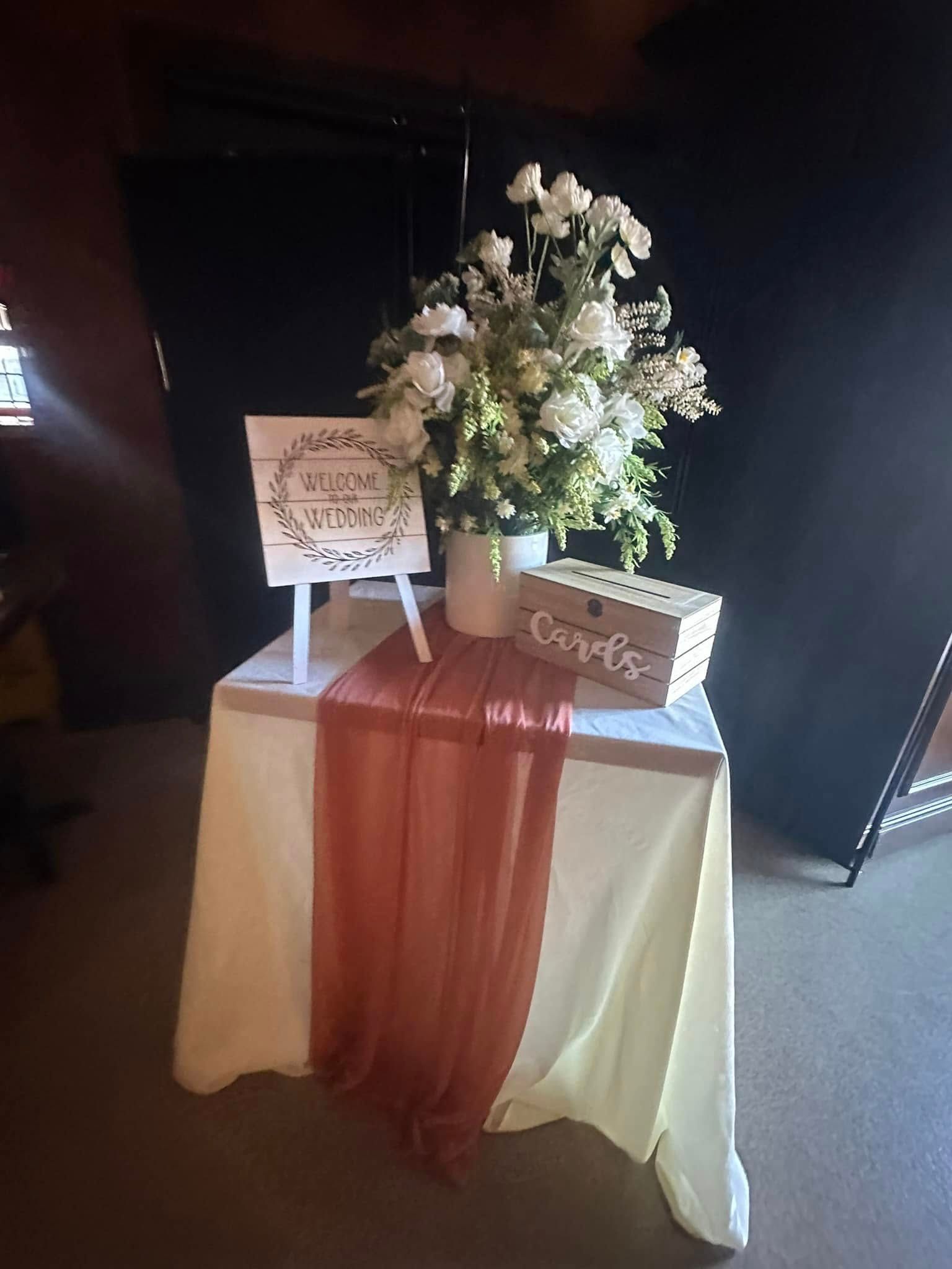 A table with flowers , a sign , and a box on it.
