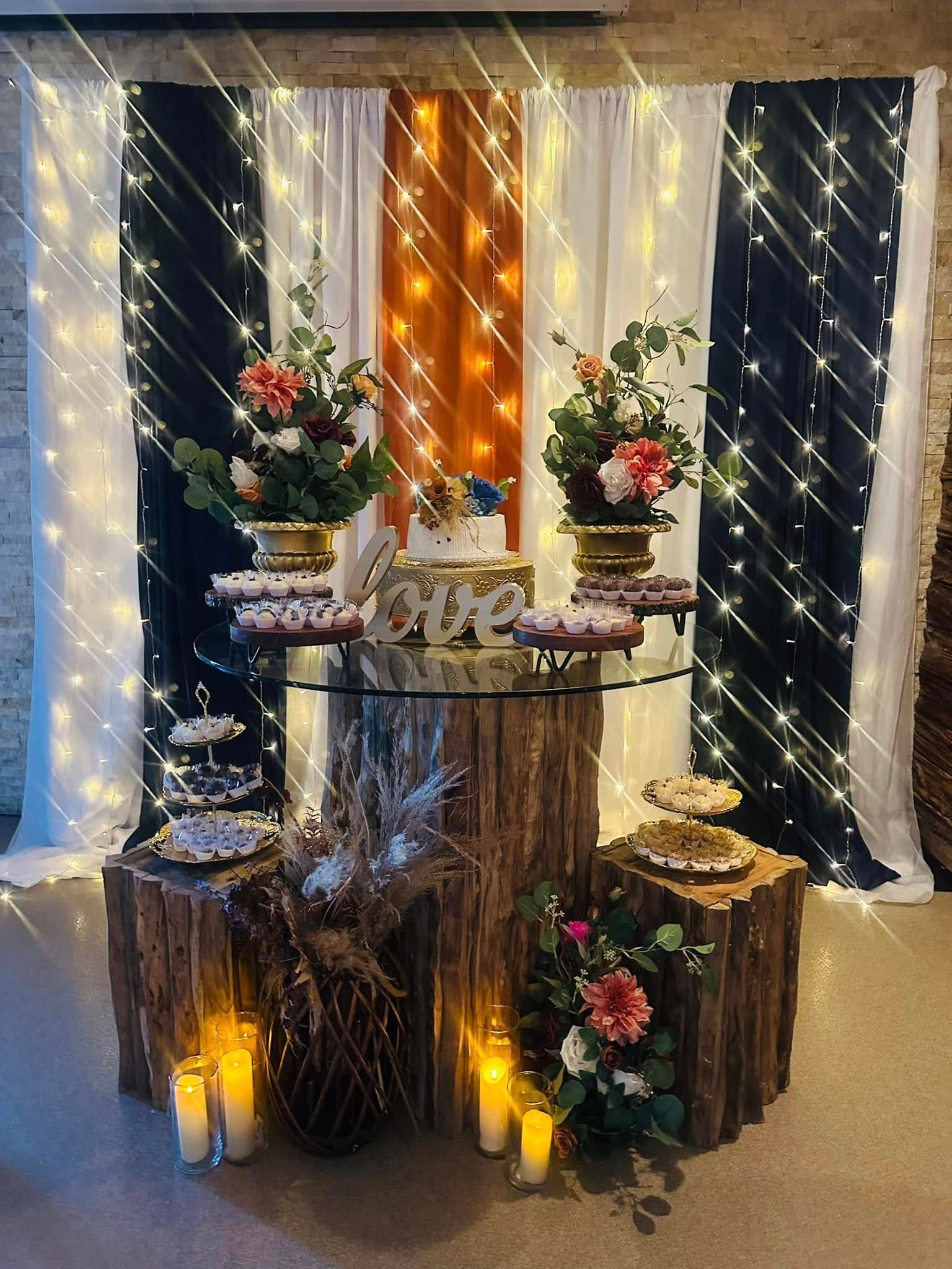 A table with candles and flowers on it in front of a curtain with lights.