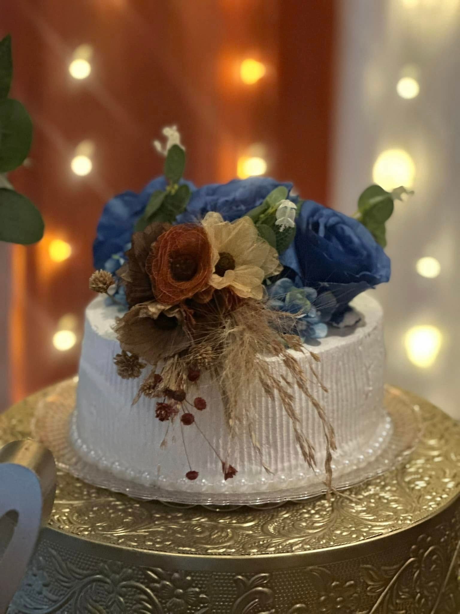 A white cake with blue flowers on top of it is sitting on top of a gold plate.