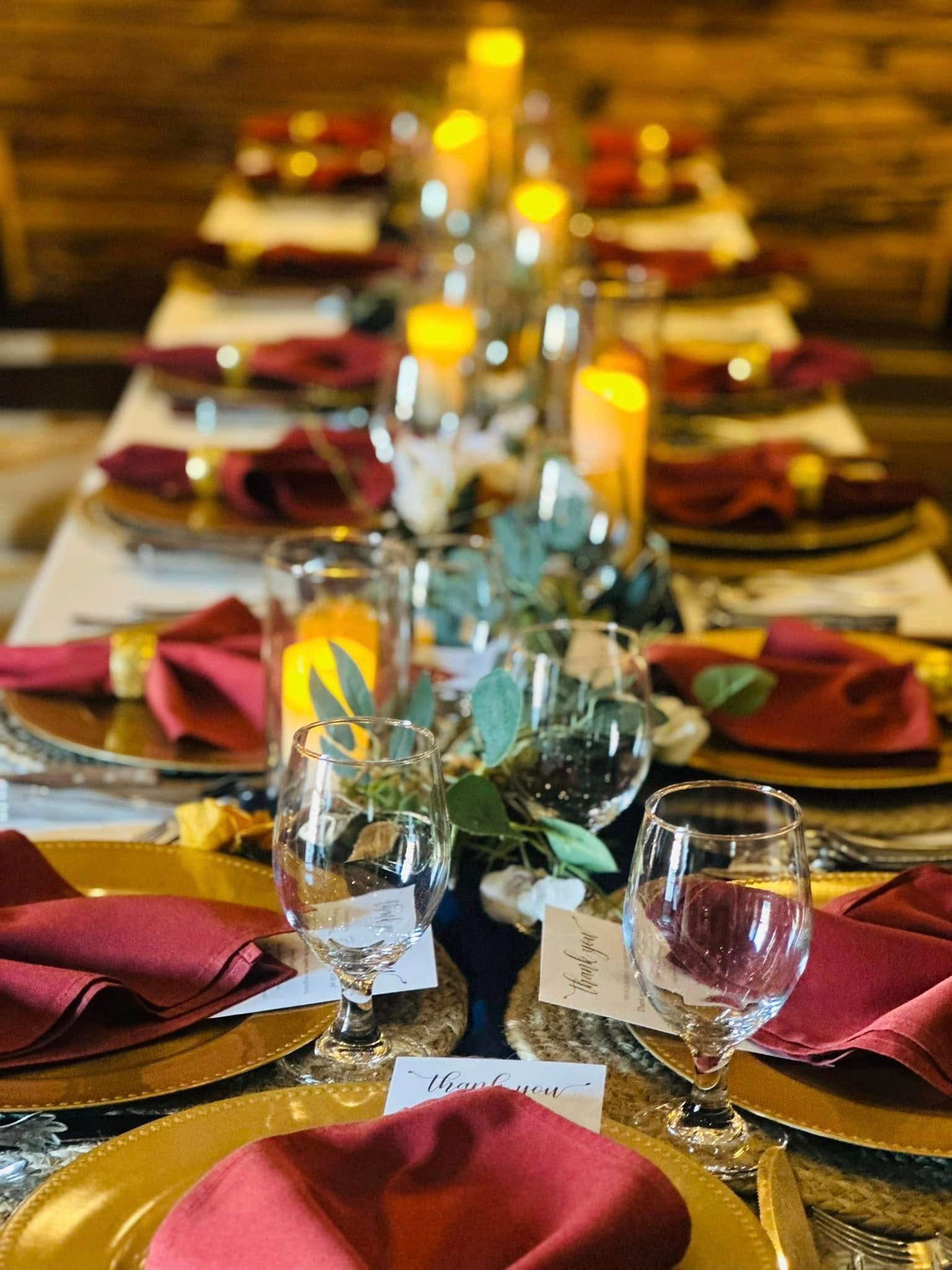A long table with plates , glasses , napkins and candles on it.
