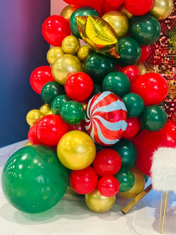 A bunch of red , green and gold balloons are sitting on a table.