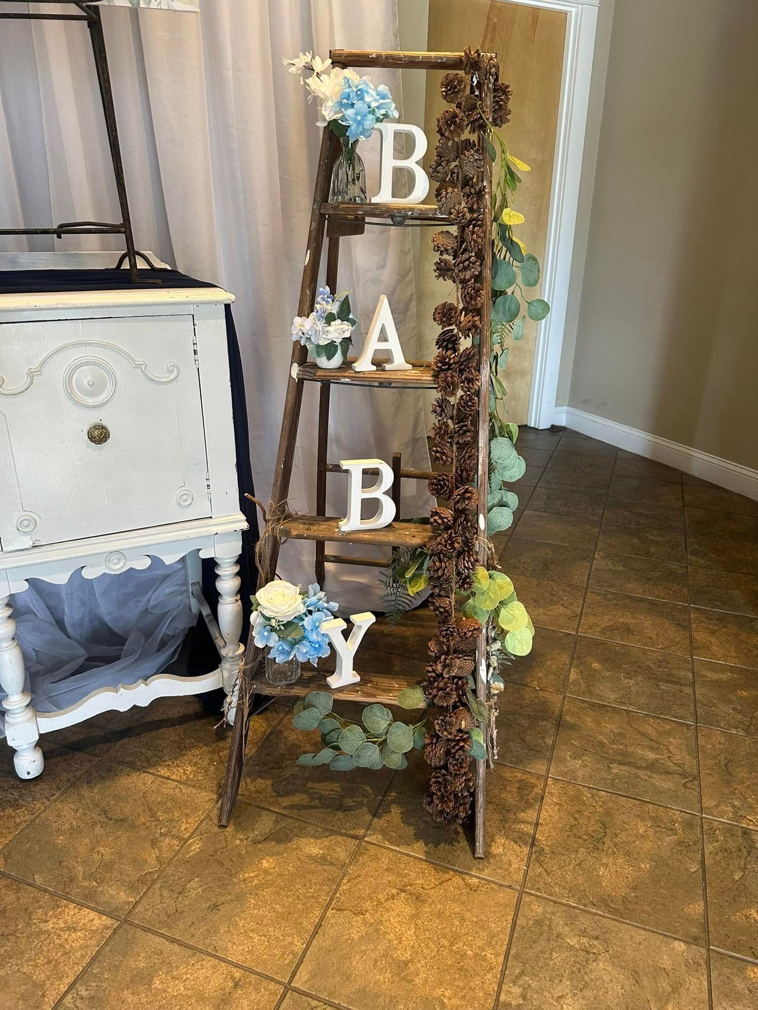 A wooden ladder is decorated with flowers and pine cones for a baby shower.