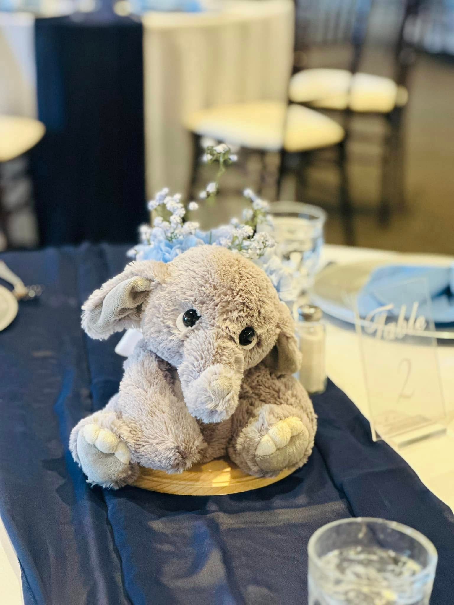 A stuffed elephant is sitting on a table next to a glass of water.