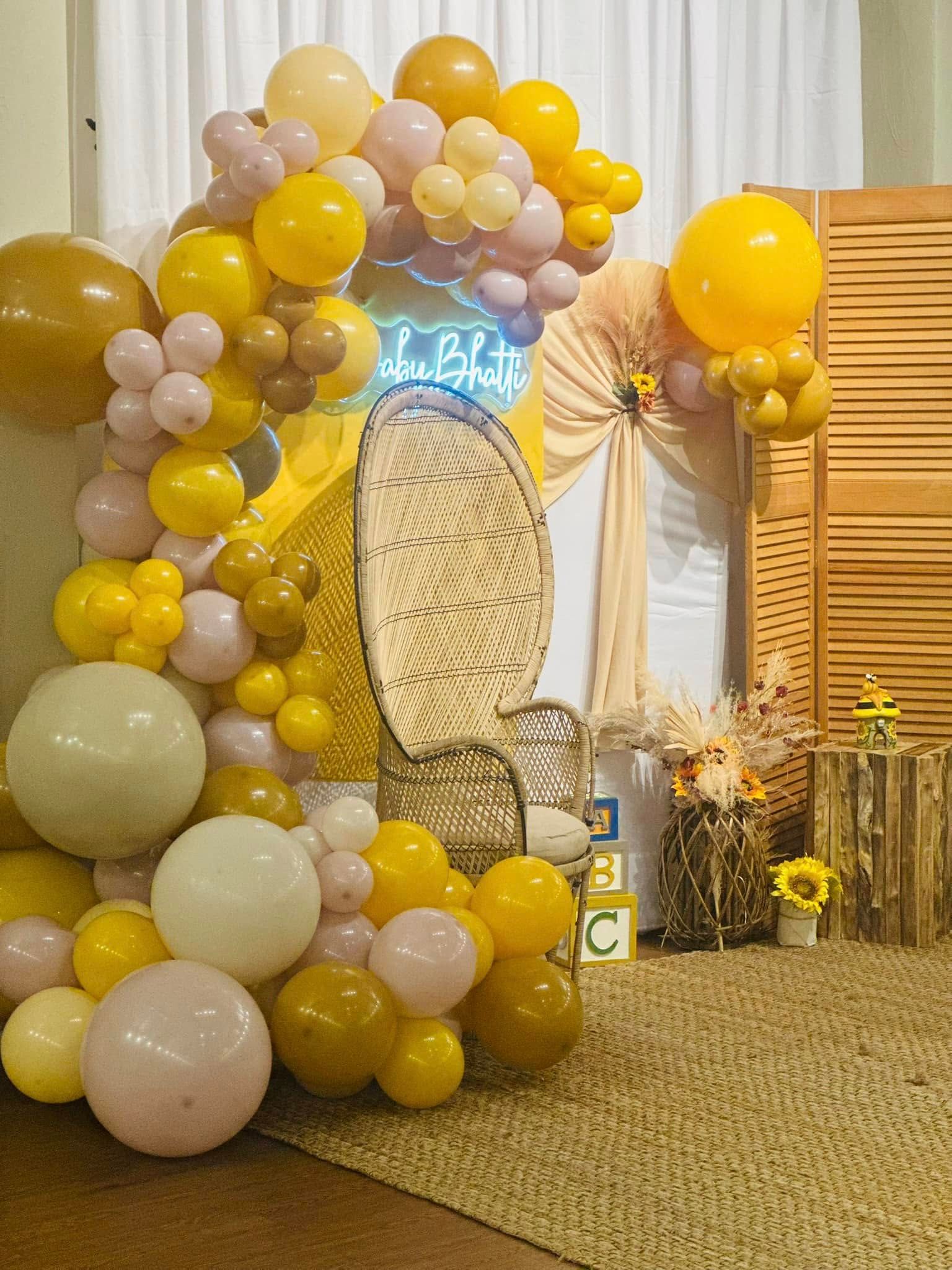 A room decorated with yellow and pink balloons and a wicker chair.