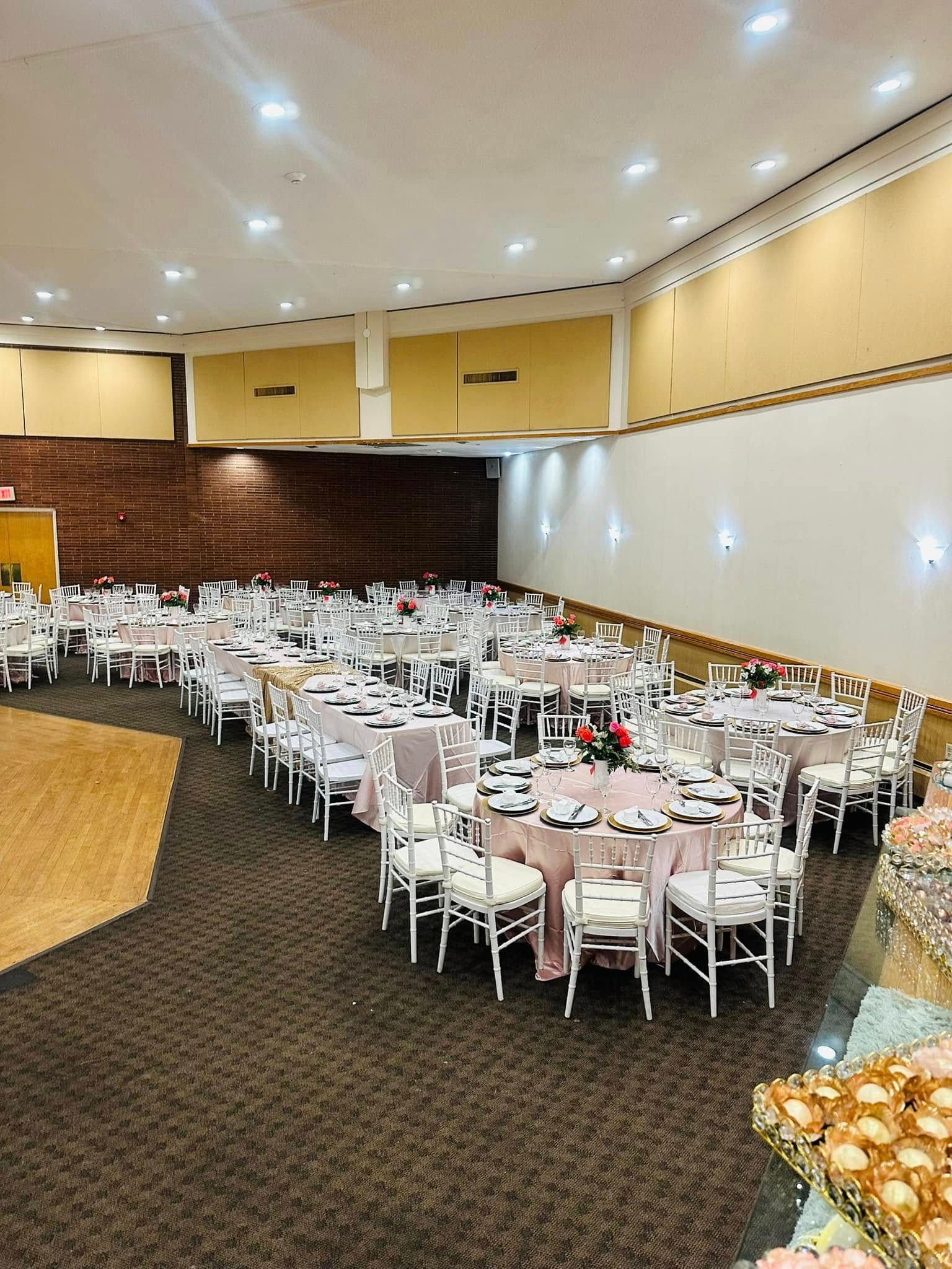 A large room filled with tables and chairs set up for a wedding reception.