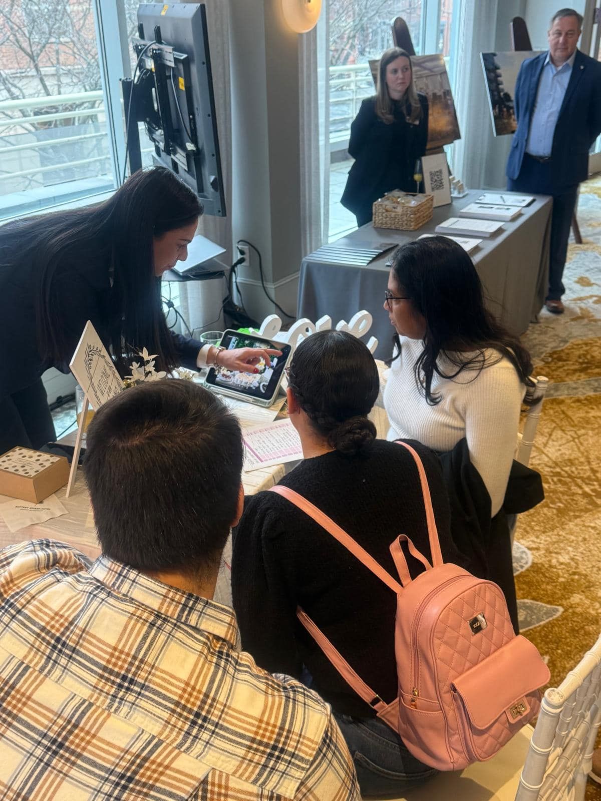 A group of people are sitting at a table with a pink backpack.