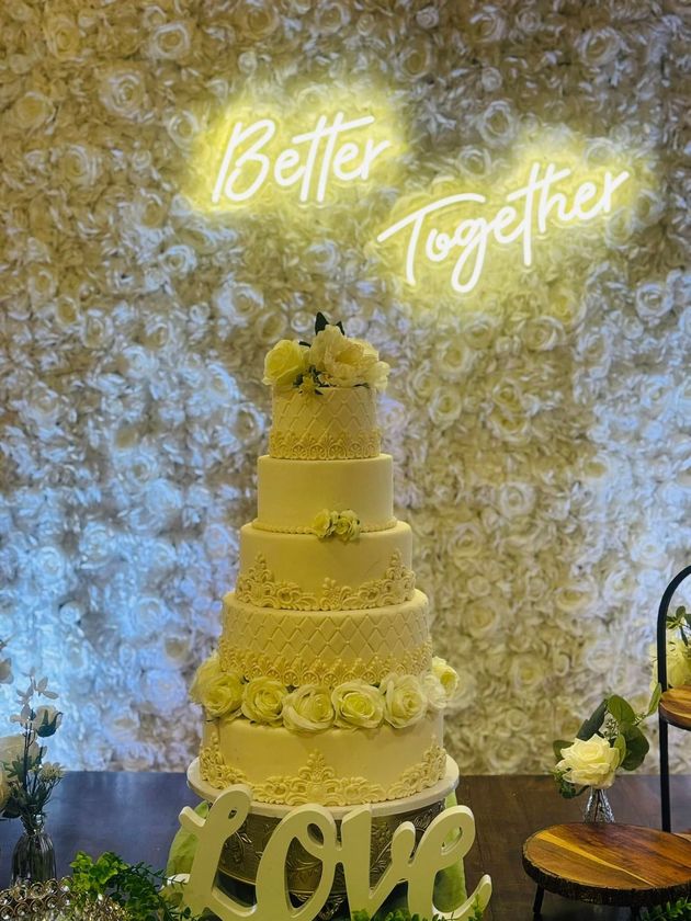 A wedding cake is sitting on a table in front of a neon sign that says `` better together ''.