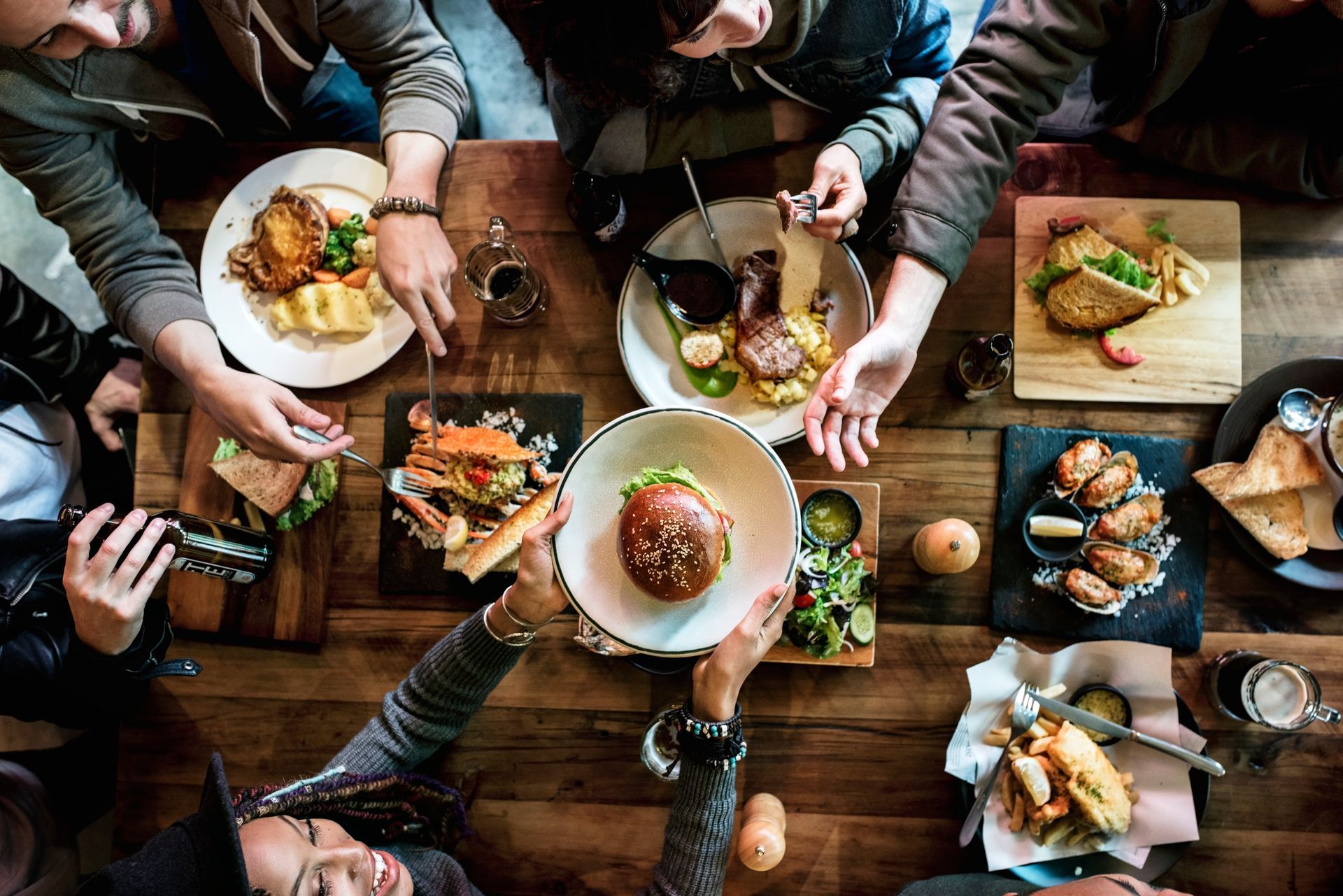 Friends sharing a meal around a wooden table, with plates of food and drinks in a cozy dining setting