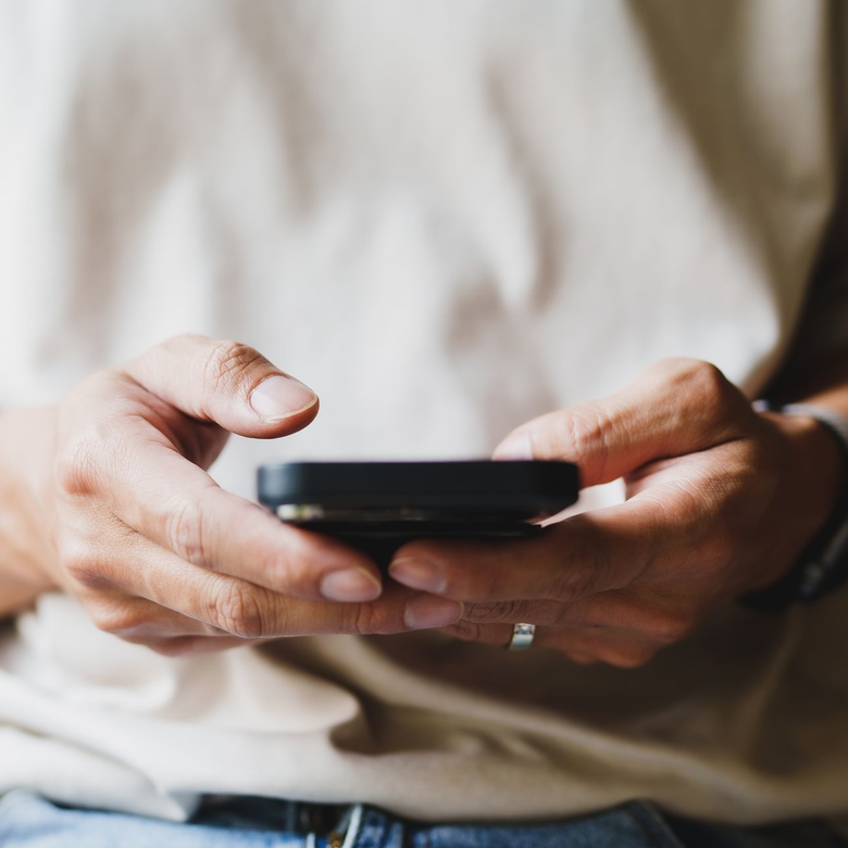 Hands holding a smartphone, typing on a black phone against a soft beige background