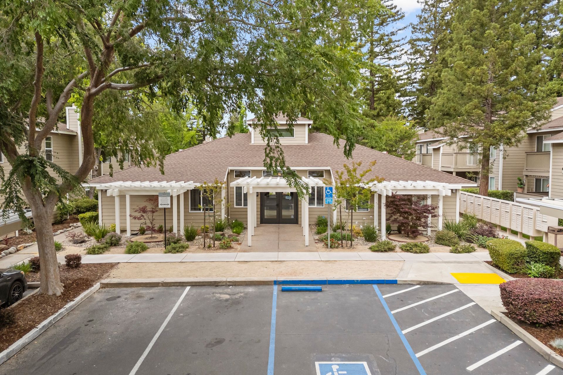 Apartment community entrance with white columns, trees, and blue-striped accessible parking spaces in front