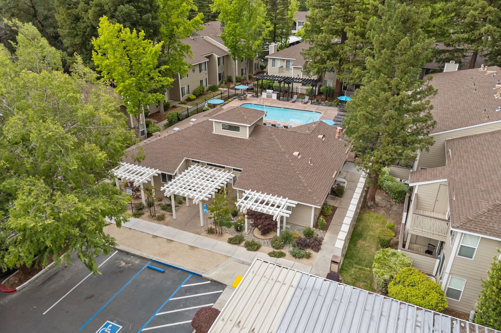 Aerial view of an apartment complex with a swimming pool, trees, and parking lot.