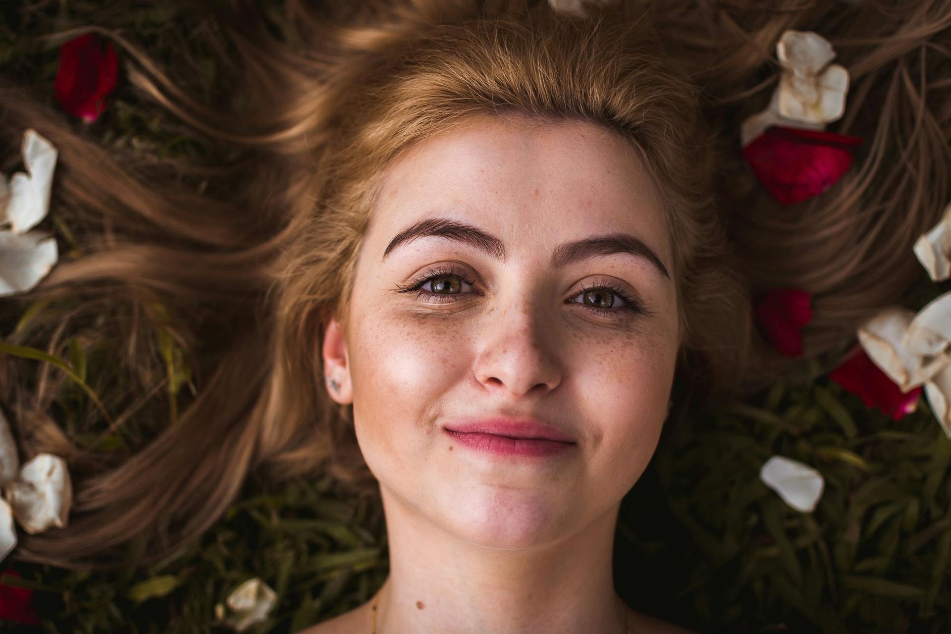 A woman is laying on the grass with petals in her hair.