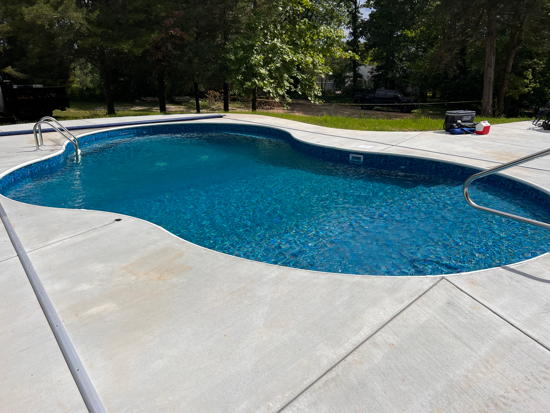 Swimming pool with blue water and concrete deck, surrounded by trees.