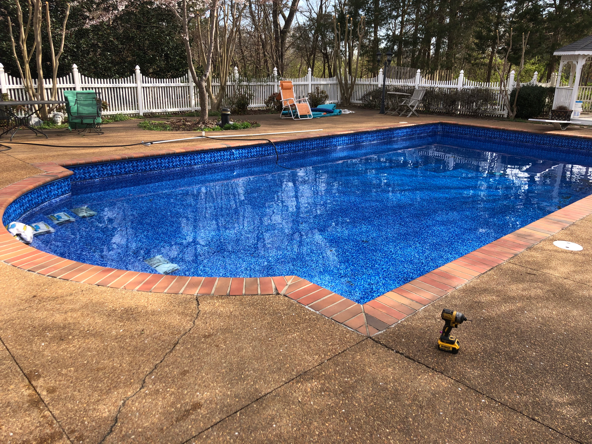 Swimming pool with blue interior and brick border surrounded by a concrete patio.