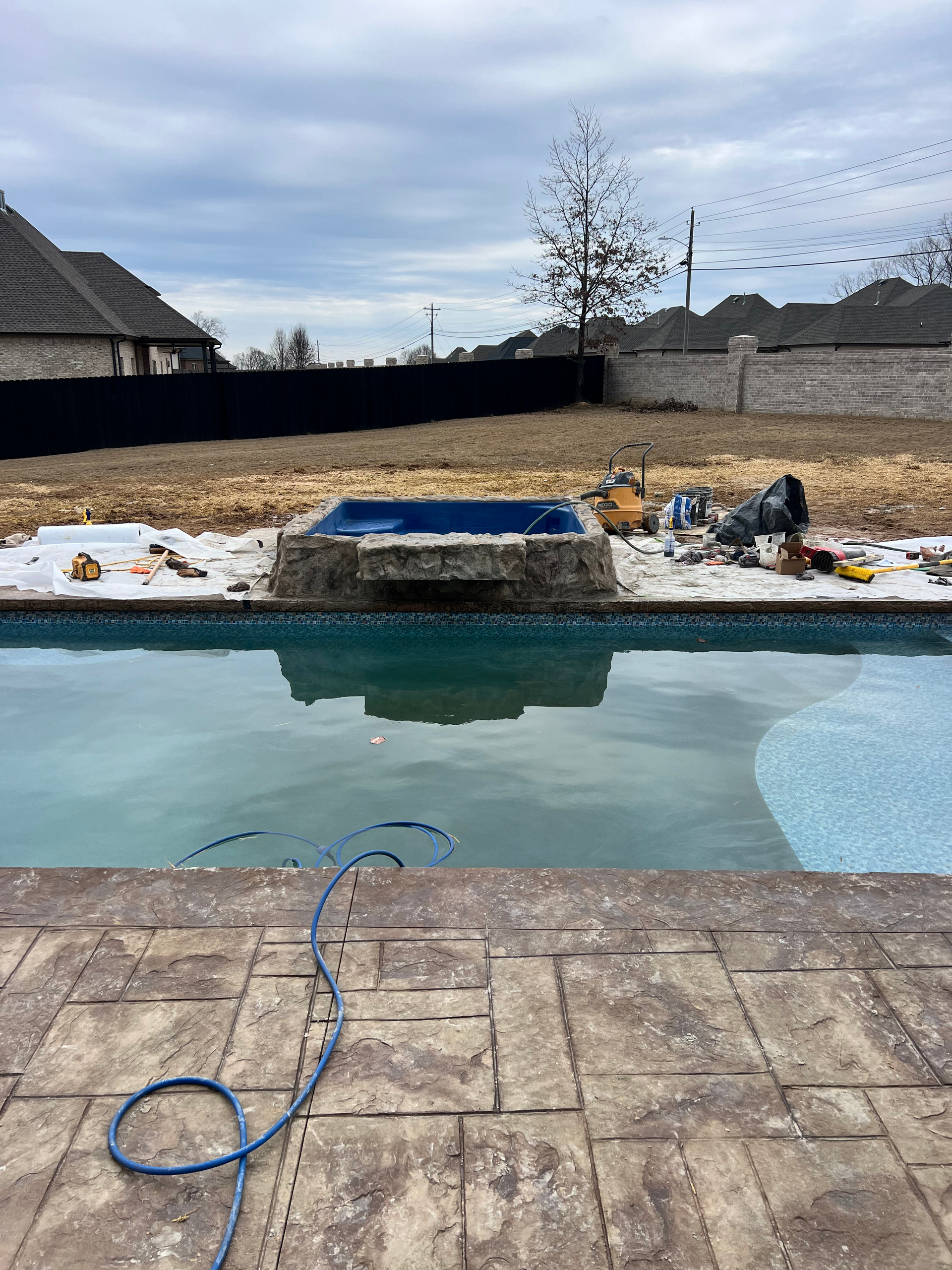 Pool with a rock waterfall under construction. Tools and building materials surround.