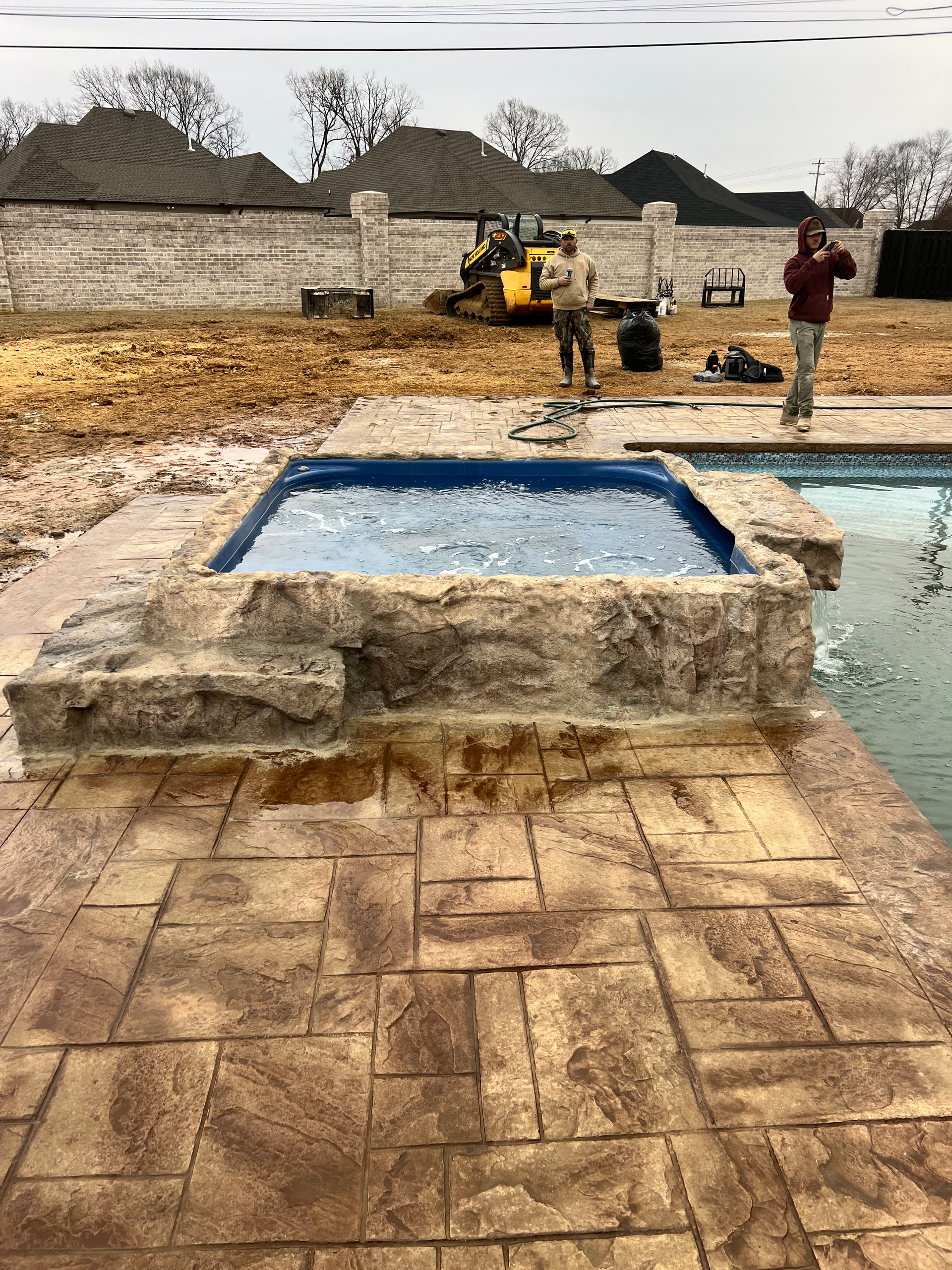 Hot tub and pool construction site with workers; stamped concrete patio.