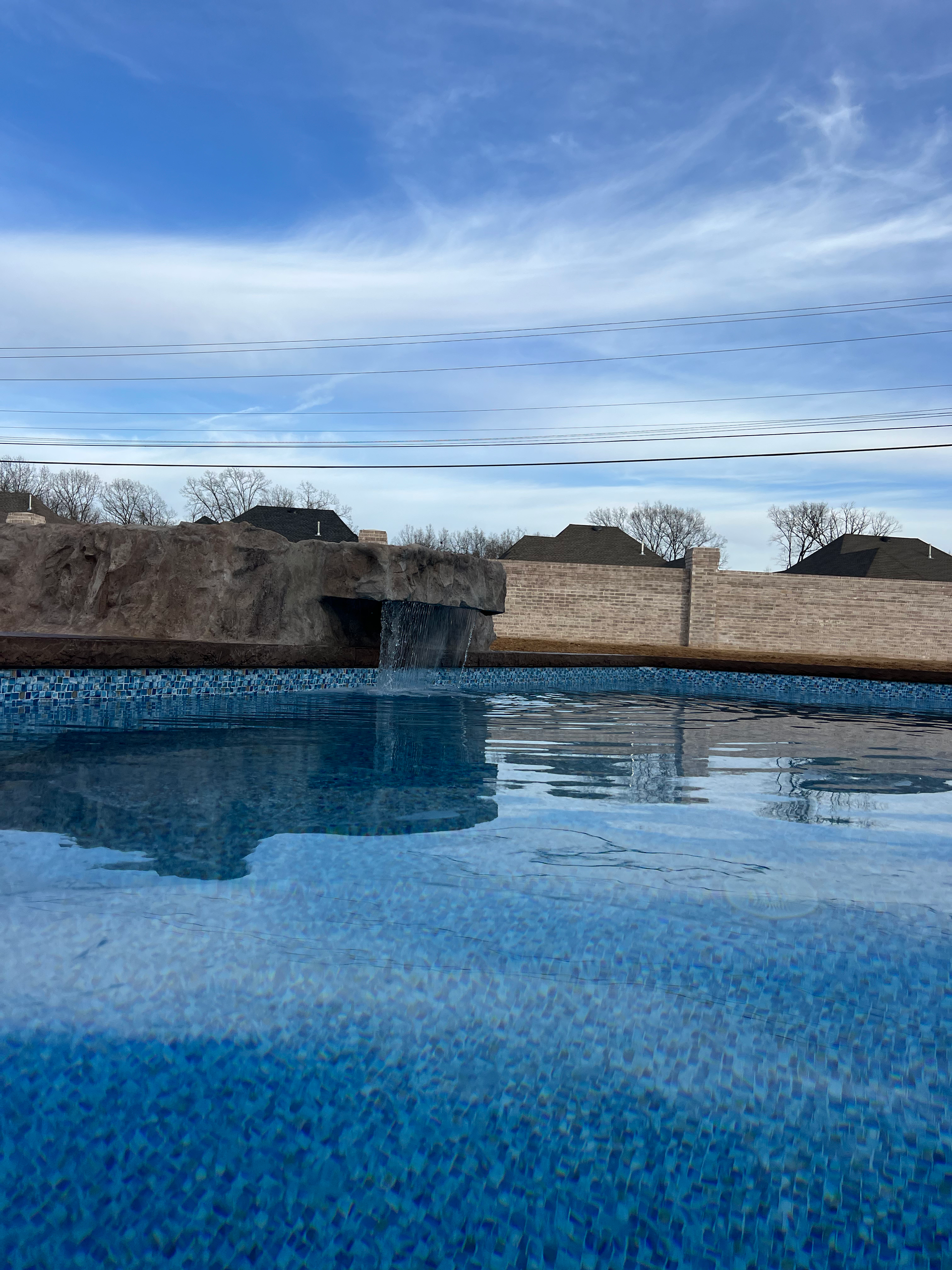 Blue pool reflecting the sky, with a stone structure and bare trees on the horizon under a cloudy sky.