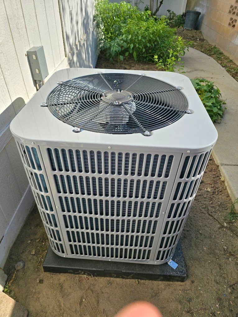 A large air conditioner is sitting in the dirt outside of a house.