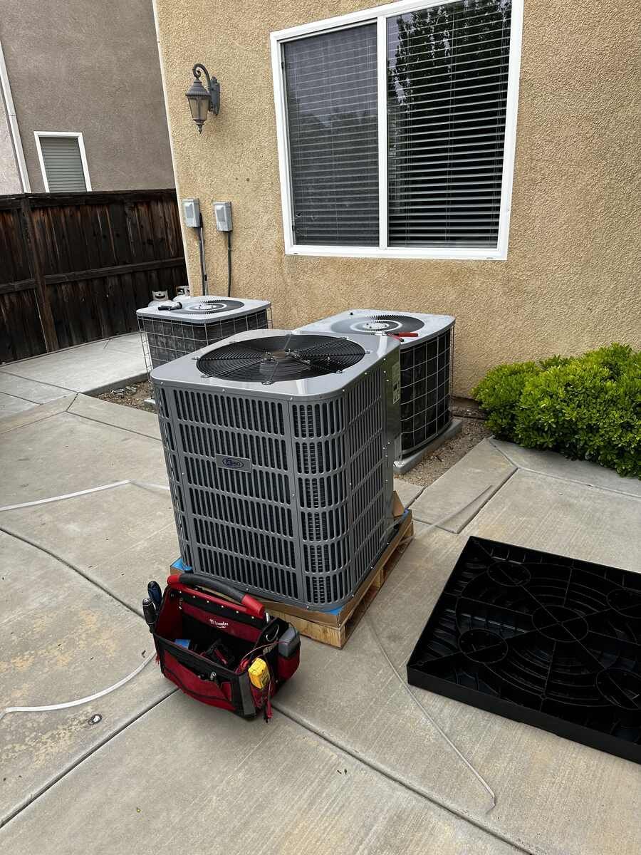 Two air conditioners are sitting on a concrete patio next to a window.