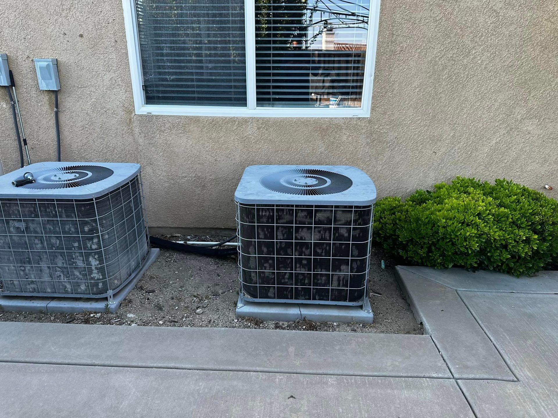 Two air conditioners are sitting outside of a building next to a window.