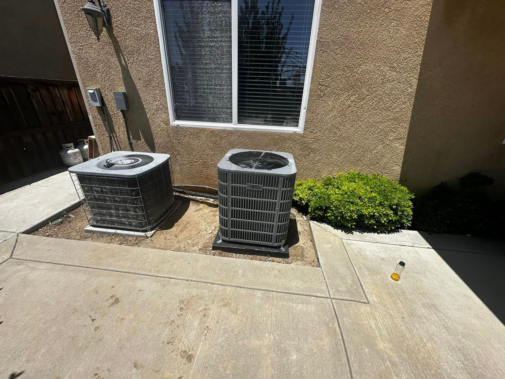 Two air conditioners are sitting on the side of a building next to a window.