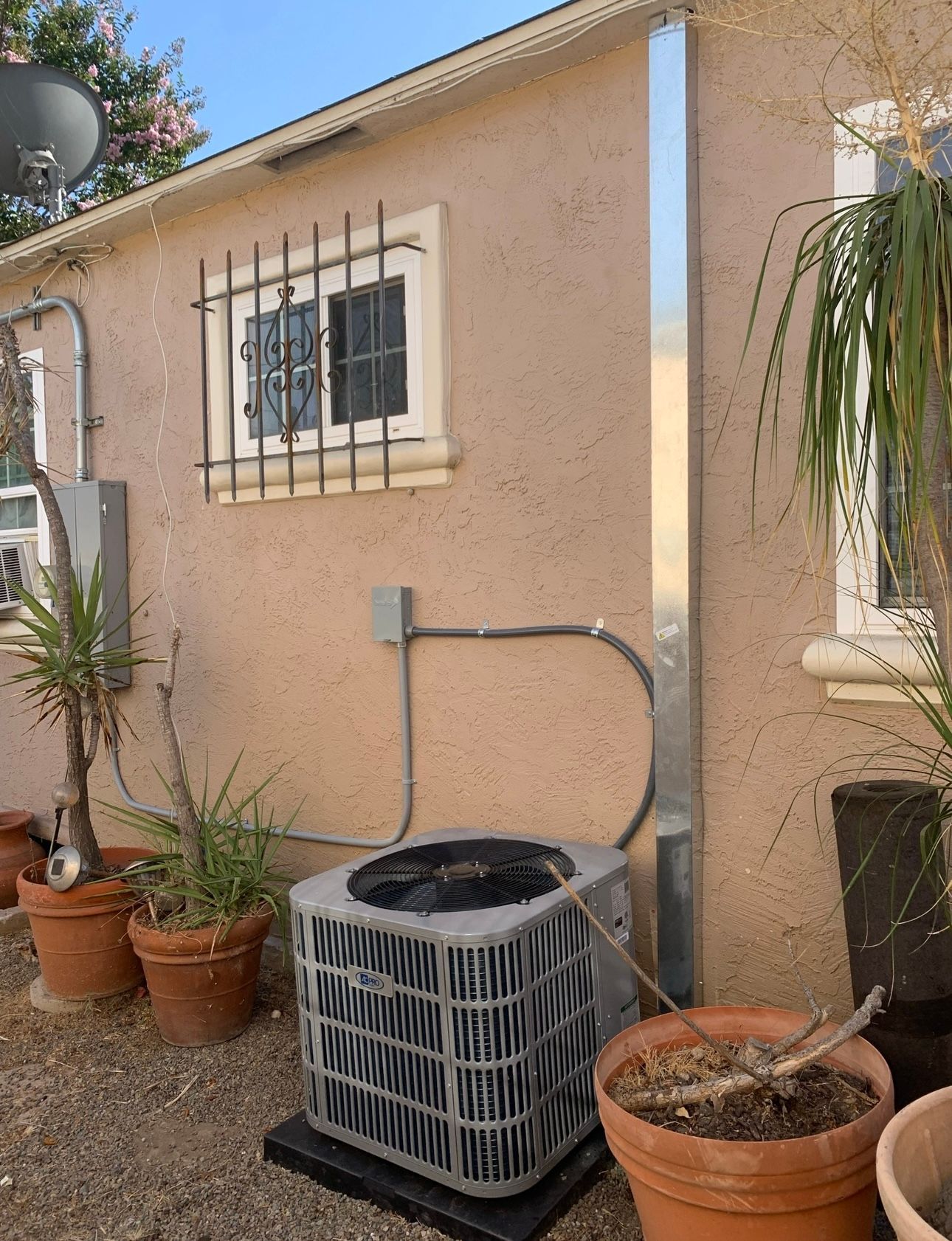 An air conditioner is sitting on the side of a house surrounded by potted plants.