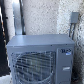 A gray air conditioner is sitting on the side of a building.