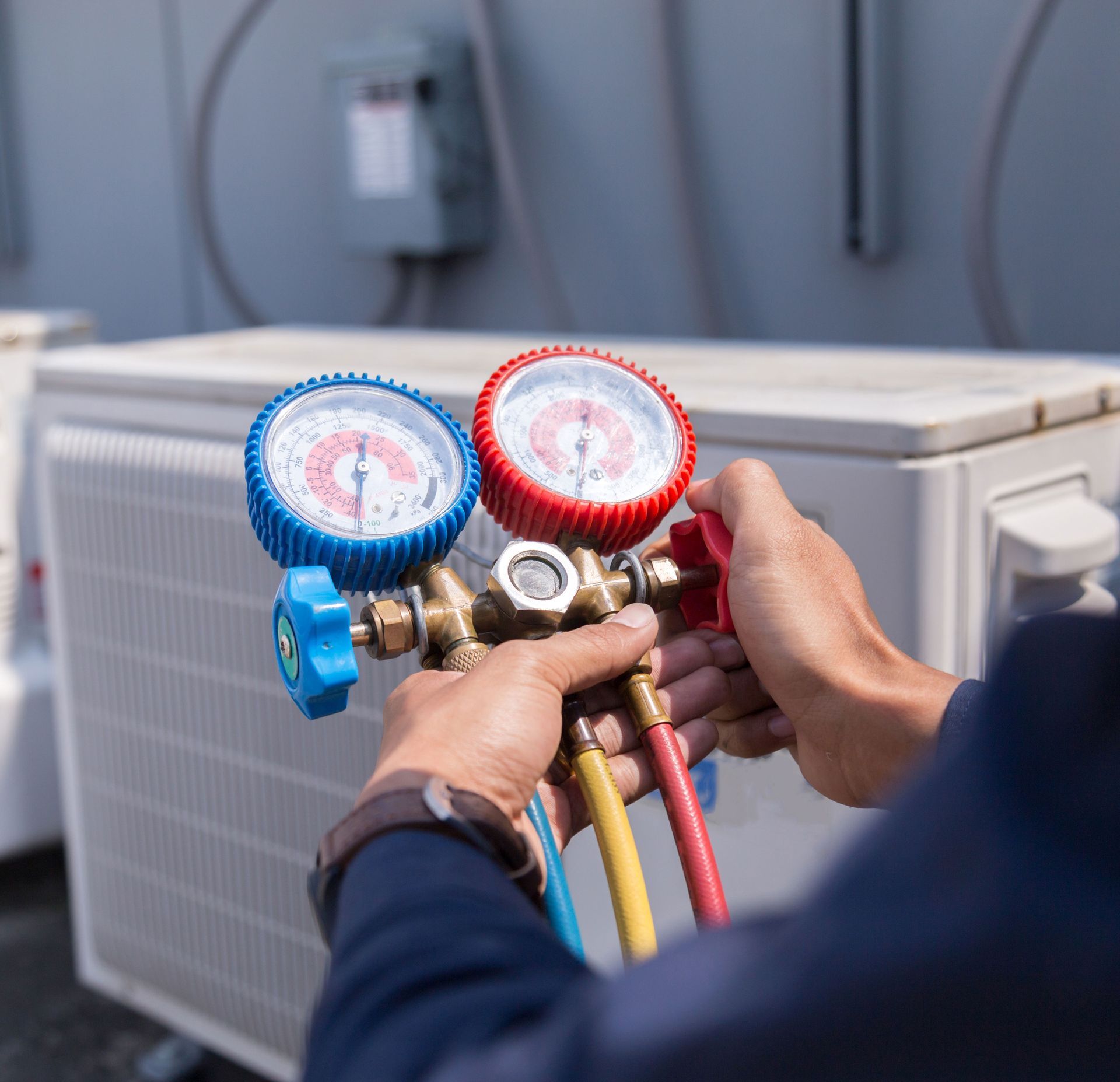 A man is holding two gauges in his hands in front of an air conditioner.