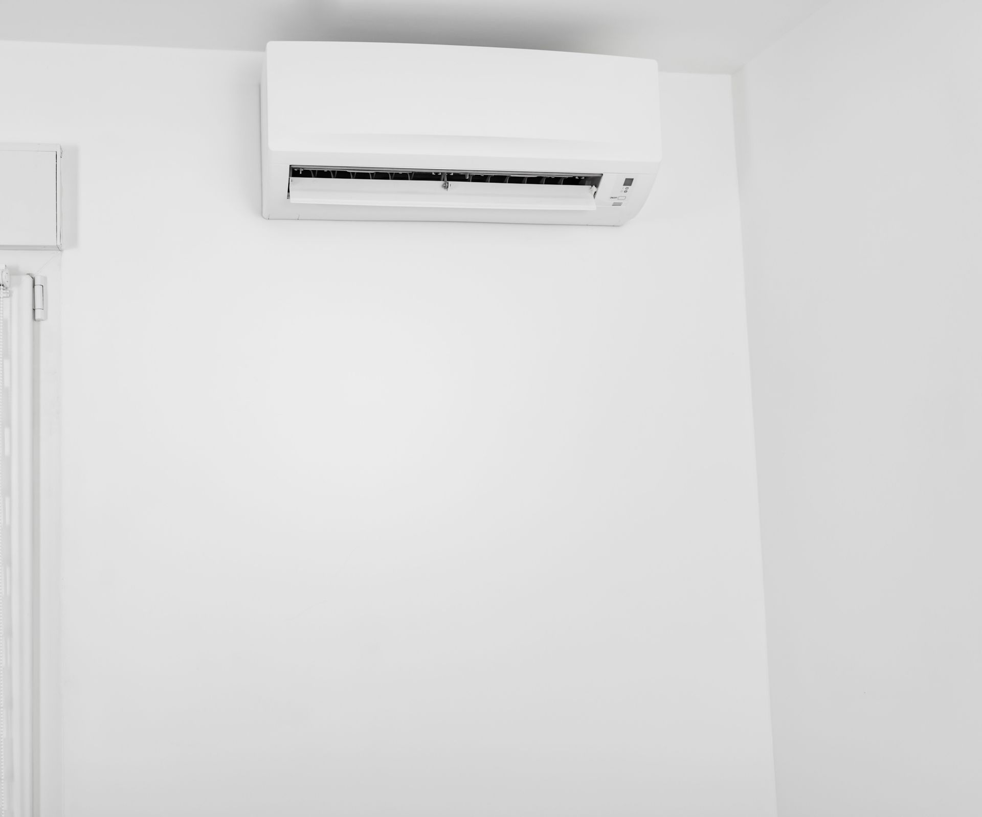 A white air conditioner is hanging on a white wall in a room.