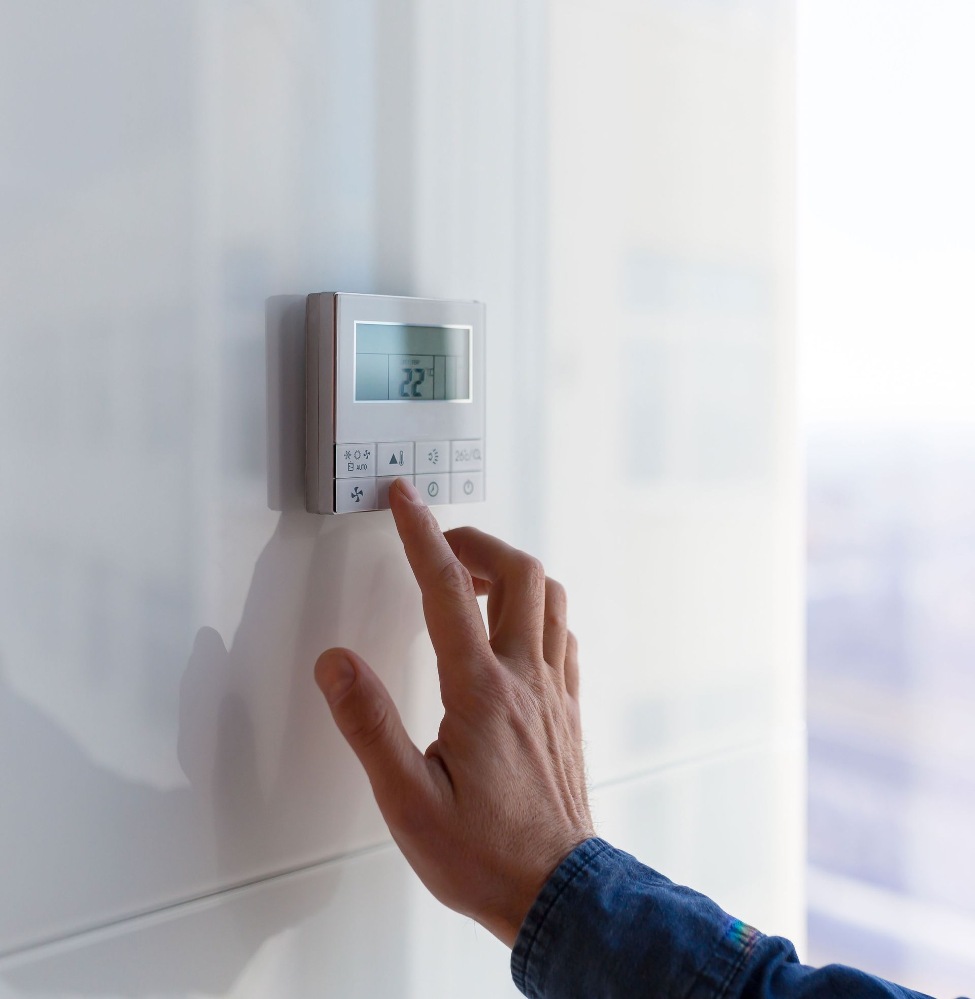 A person is pressing a button on a thermostat.