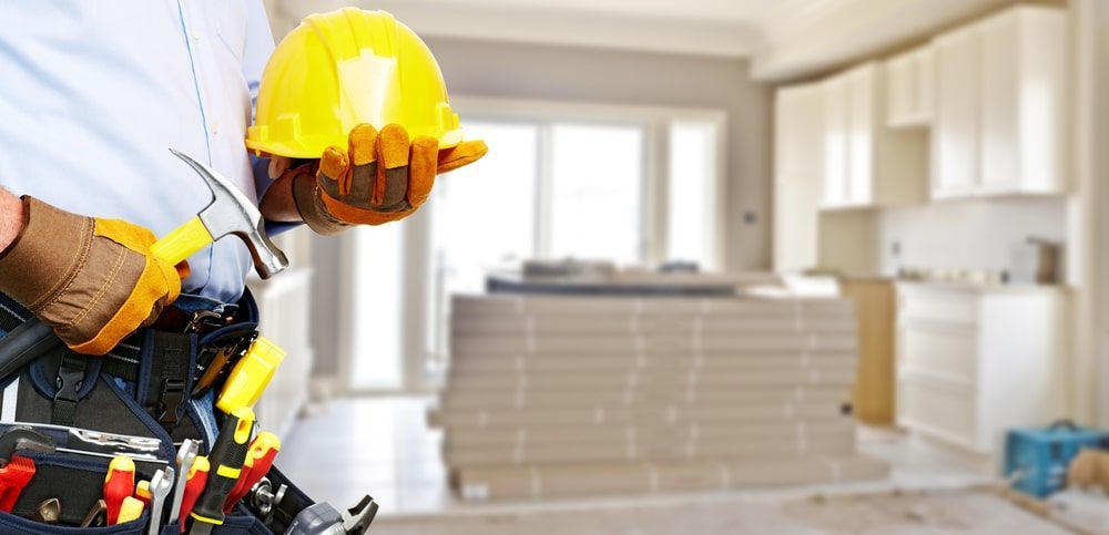 Construction Worker Holding A Hard Hat And A Hammer In A Kitchen — R3 Construction In Canberra, ACT