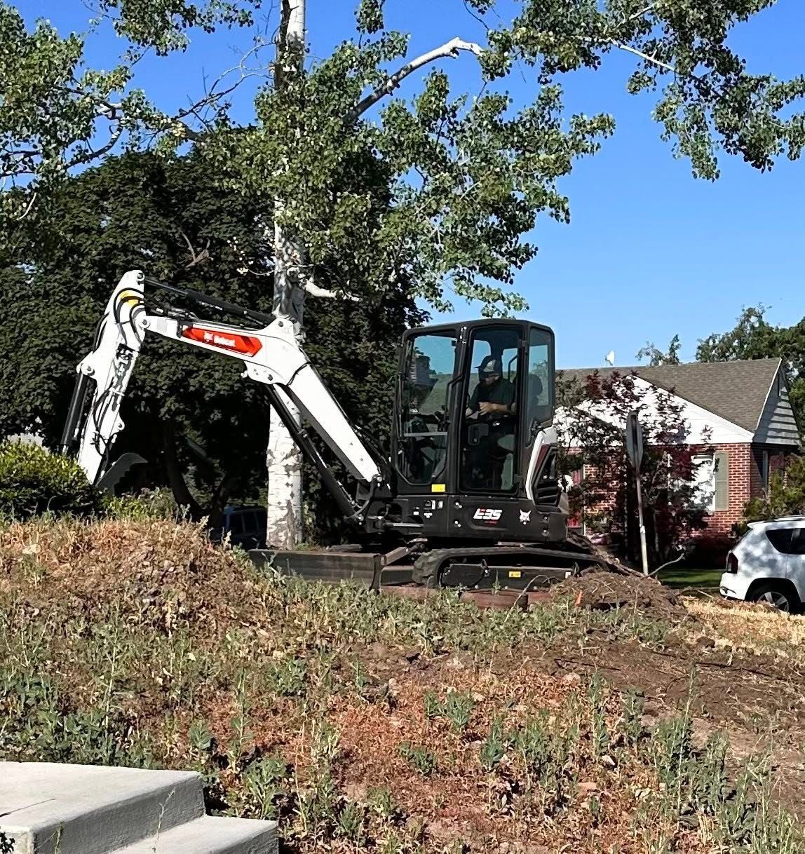 A Bobcat excavator removing a tree in a residential yard on a sunny day.