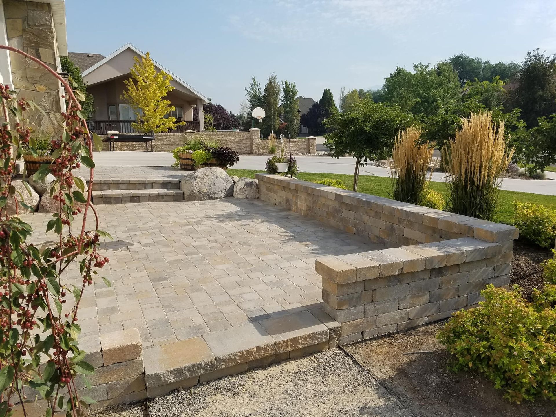 Stone patio with low retaining walls. A house, trees, and landscaping are in the background.