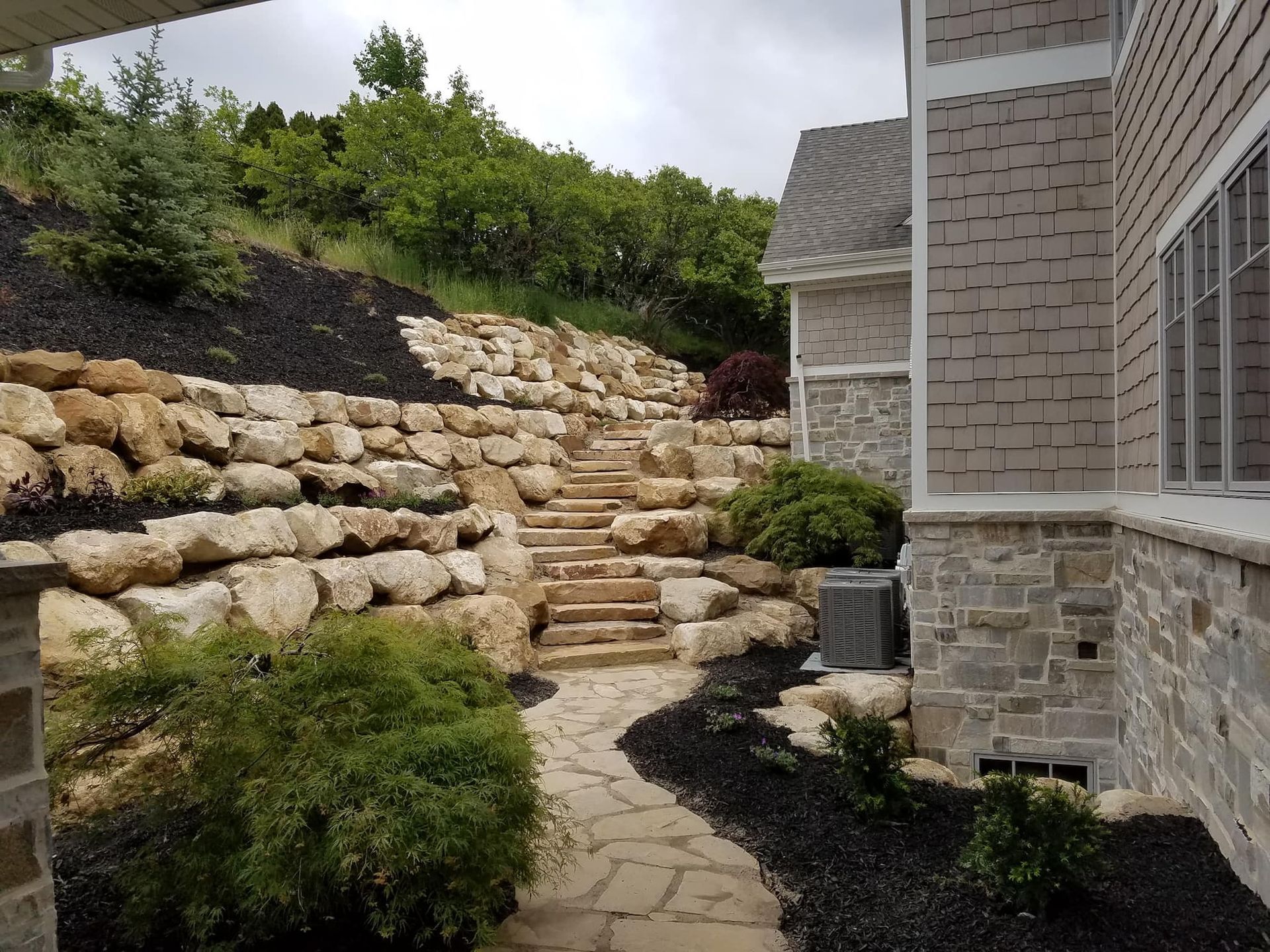 Stone steps and pathway leading up a rocky hillside with landscaping and a house.