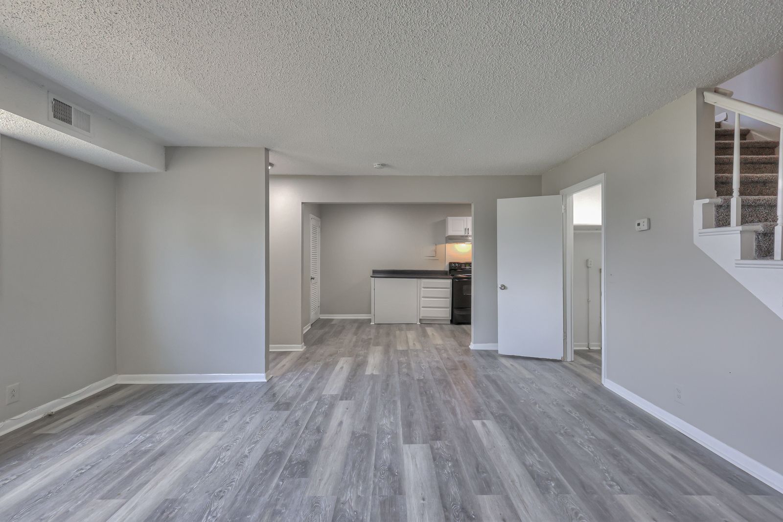 Photo of a living room, with the kitchen in the background and stairs to the side