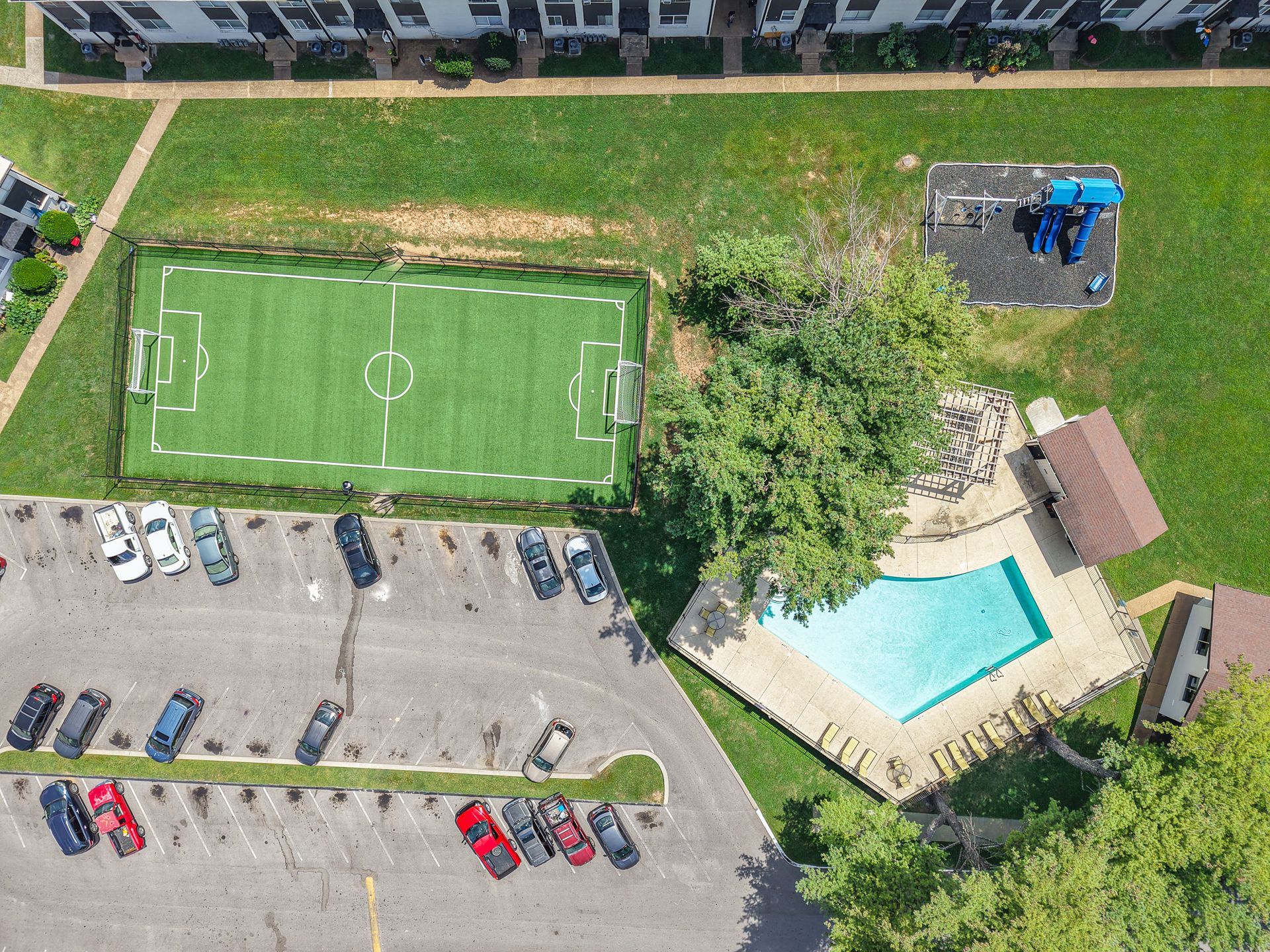 Aerial photo of a community soccer field, pool and playground, with the parking lot next to this park area