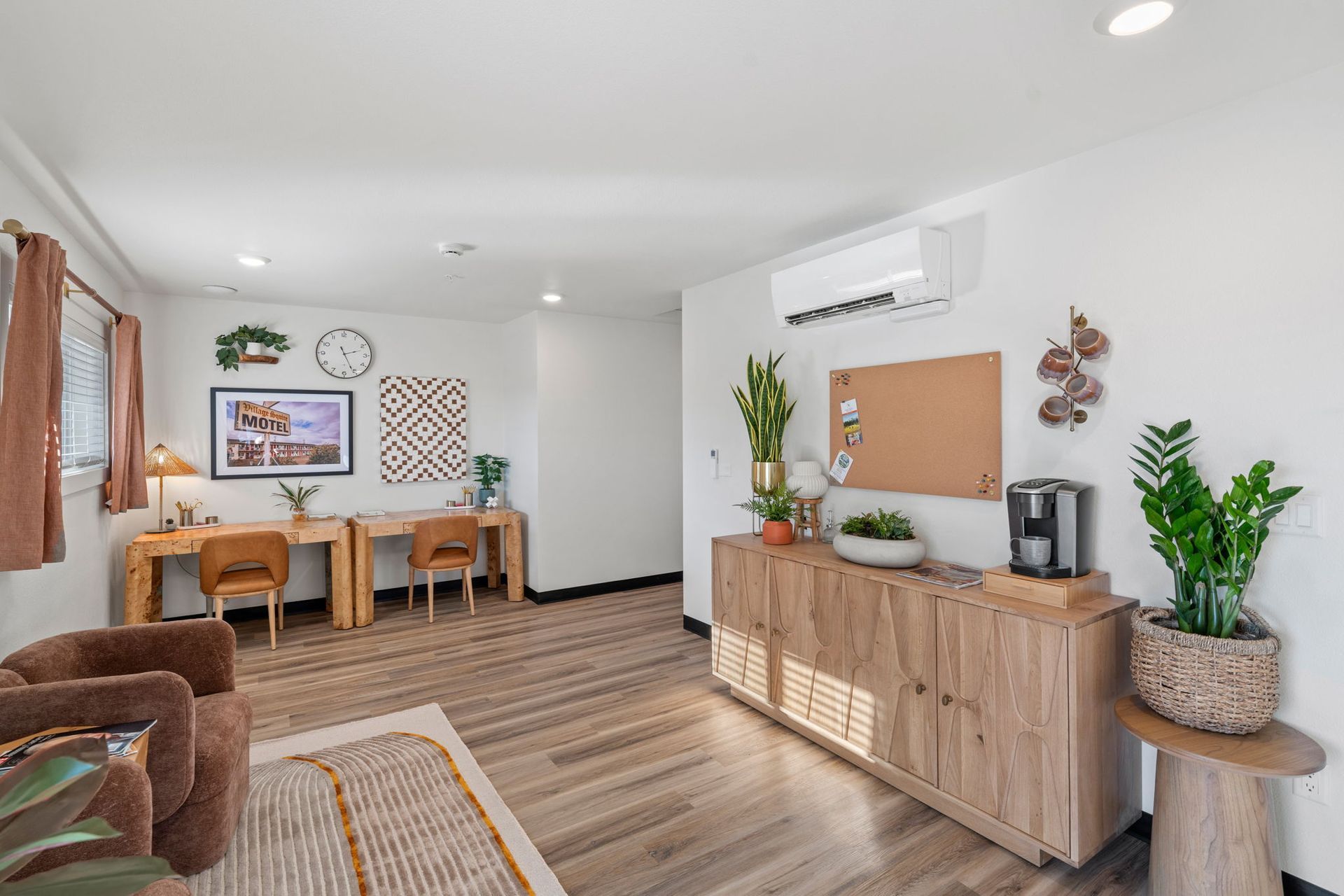 A living room with wooden floors , two desks , a chair , and a dresser.